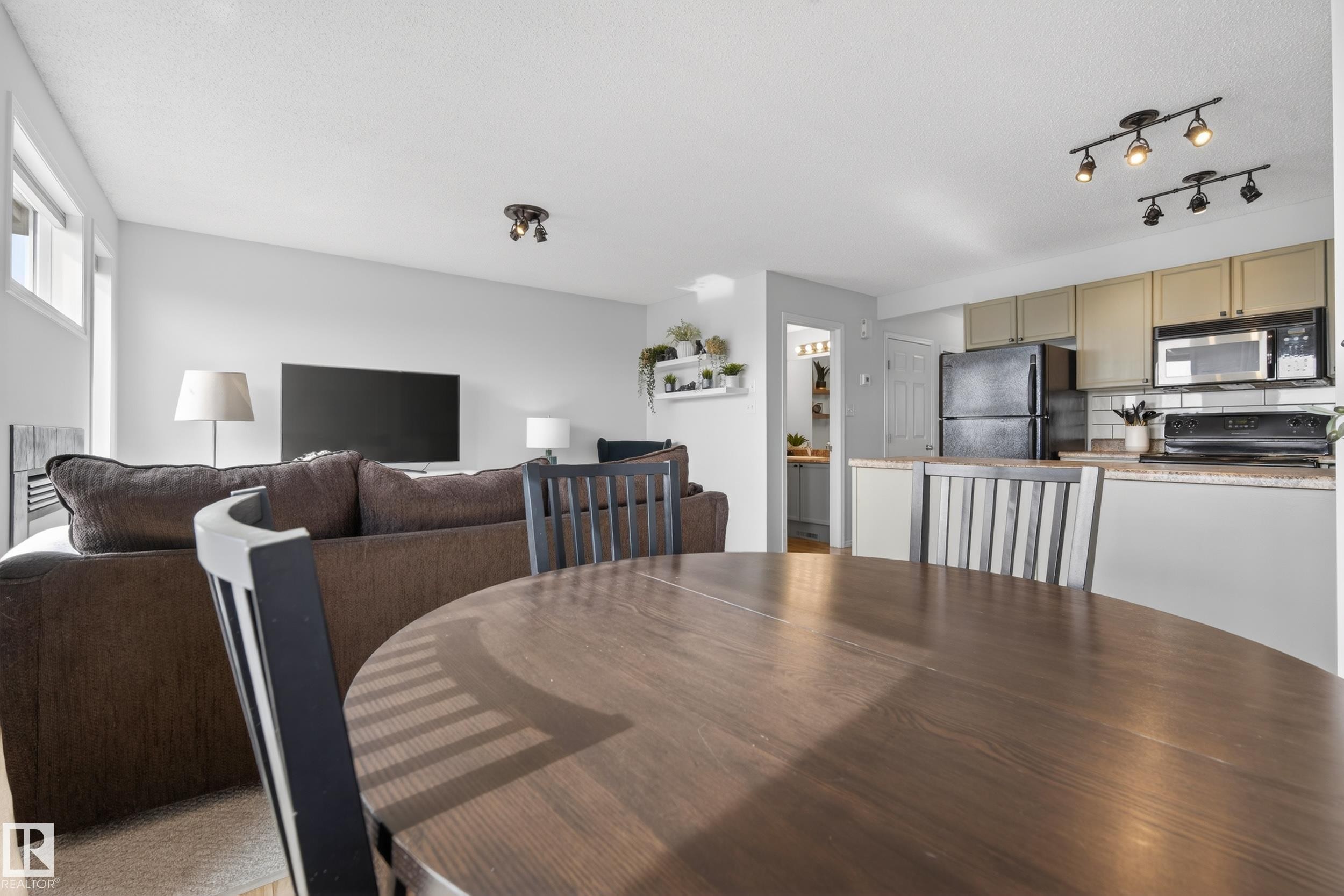 The property offers an open concept living area, featuring a dining space with a round wooden table, a living room with light-colored walls, and a kitchen equipped with a black refrigerator and microwave - 9051 Scott Crescent, Edmonton, AB