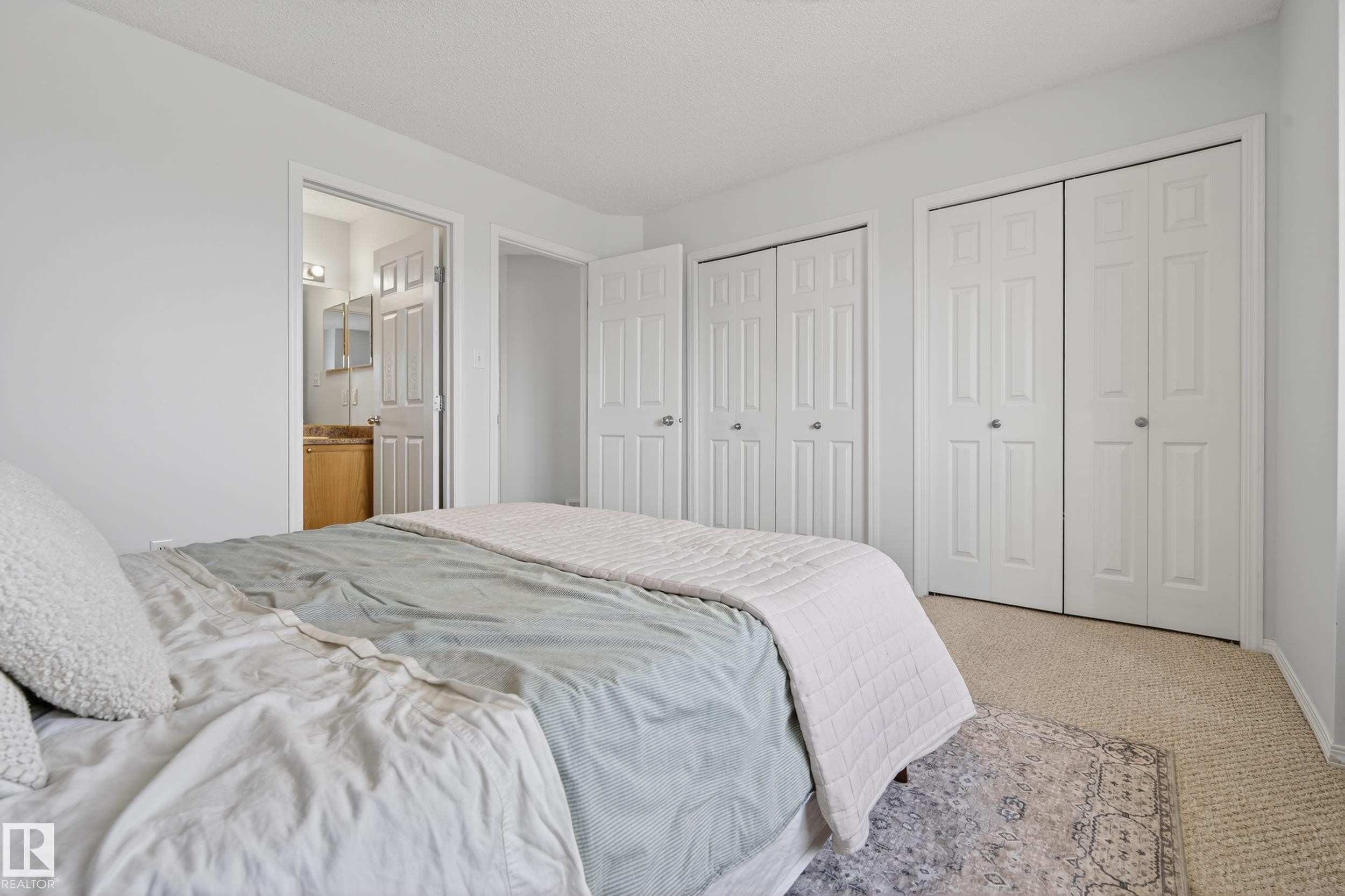 This bedroom features light-colored carpeting, white walls, and multiple white closet doors - 9051 Scott Crescent, Edmonton, AB