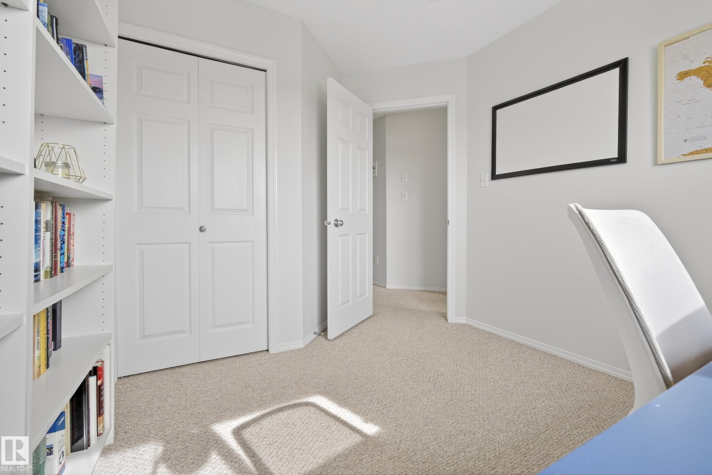 Bright room featuring neutral carpeting and light-colored walls, with a white bookshelf and closet doors - 9051 Scott Crescent, Edmonton, AB
