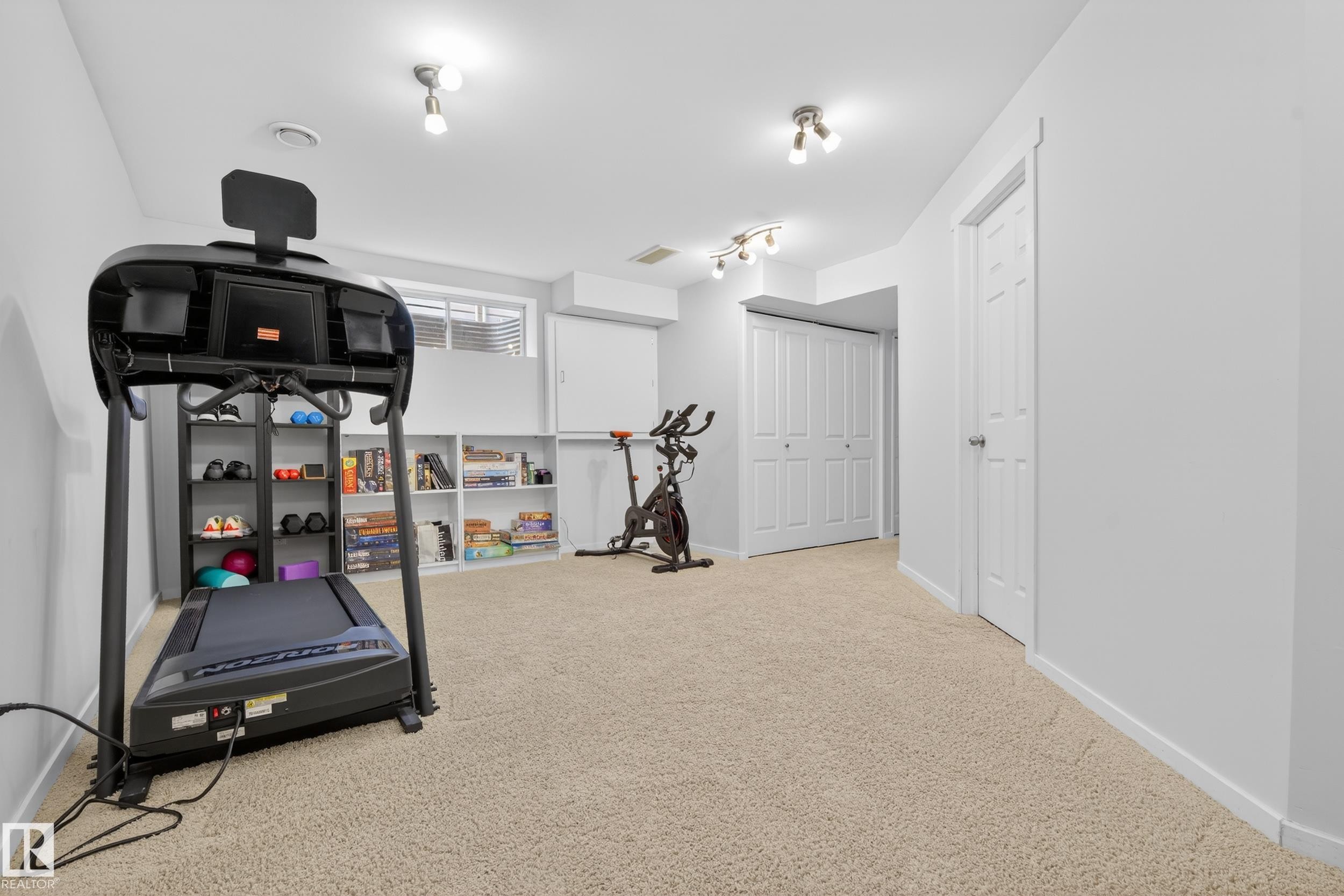 Spacious room with light-colored carpeting, multiple light fixtures, and white walls - 9051 Scott Crescent, Edmonton, AB