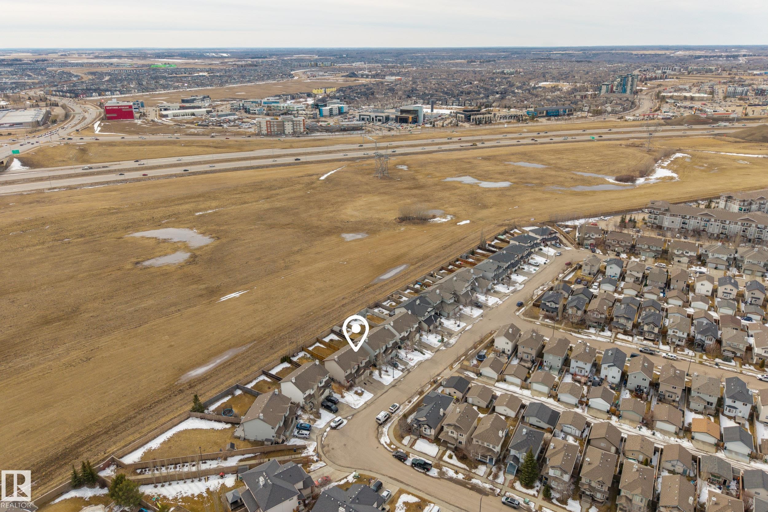 An aerial view showcasing the property within a residential development, featuring a road and nearby highway access, surrounded by expansive undeveloped land - 9051 Scott Crescent, Edmonton, AB