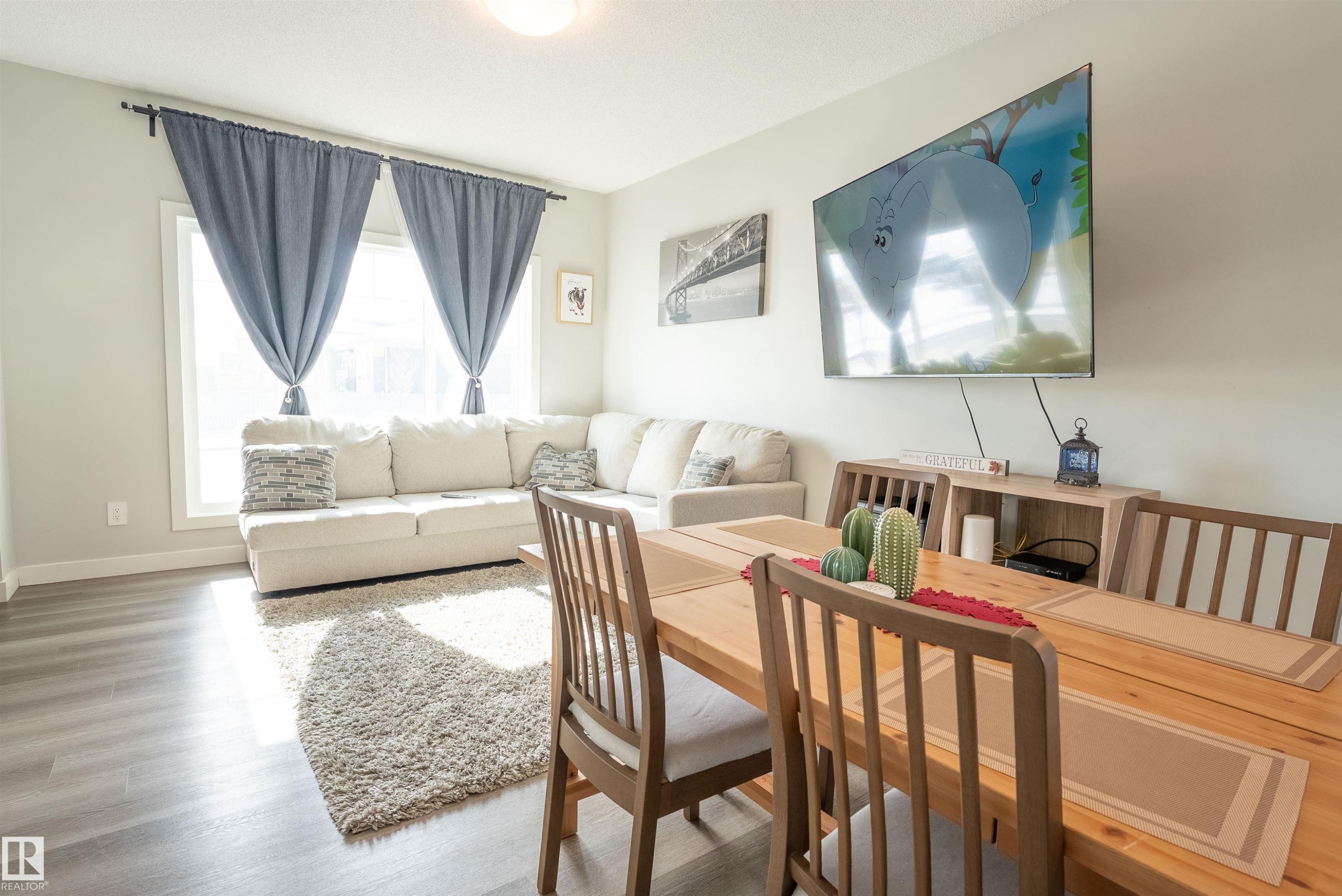 The living and dining areas feature light-toned flooring, a window with curtains, and a mounted television - 656 Black Stone, Leduc, AB - Indoor