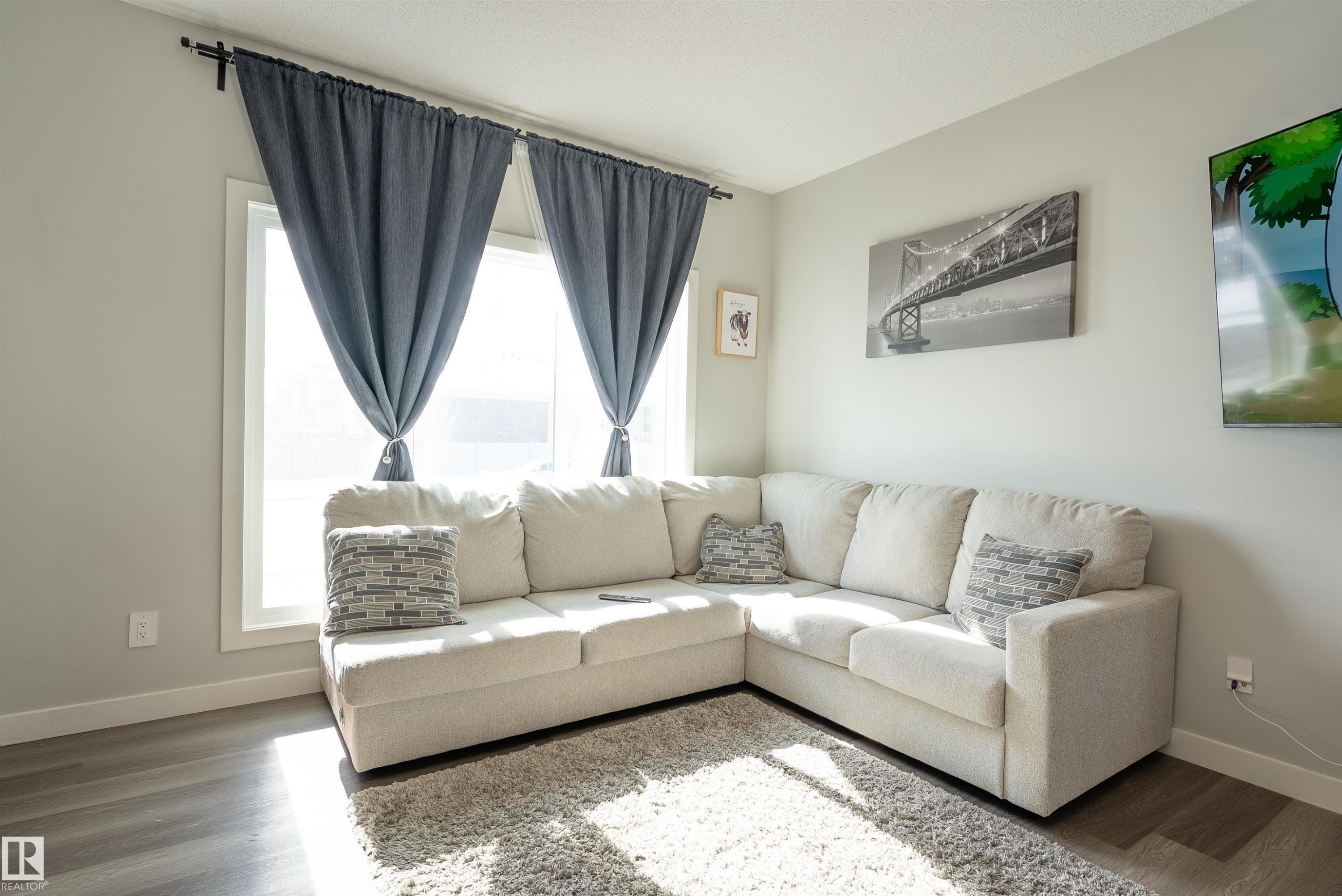 This living area features light-colored walls and dark wood-style flooring, complemented by two windows with dark blue curtains - 656 Black Stone, Leduc, AB - Indoor Photo Showing Living Room