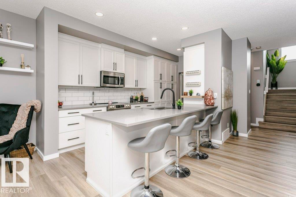 The kitchen features a large island with seating, white cabinetry, a subway tile backsplash, and stainless steel appliances - 320 Balsam Link, Leduc, AB - Indoor Photo Showing Kitchen With Upgraded Kitchen