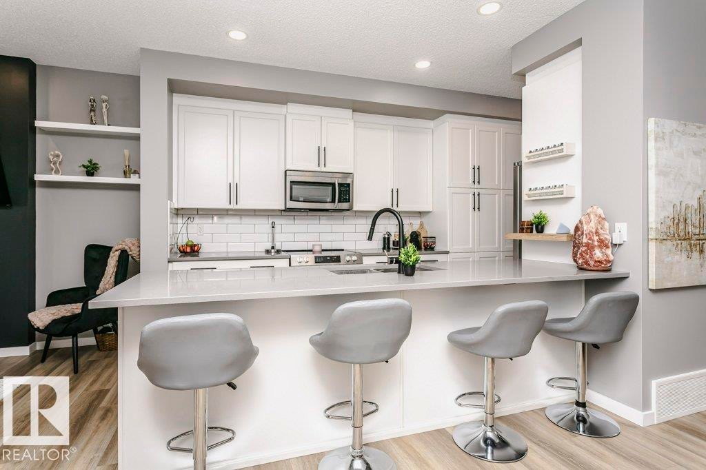 Modern kitchen featuring white cabinetry, a subway tile backsplash, and a large island with seating - 320 Balsam Link, Leduc, AB - Indoor