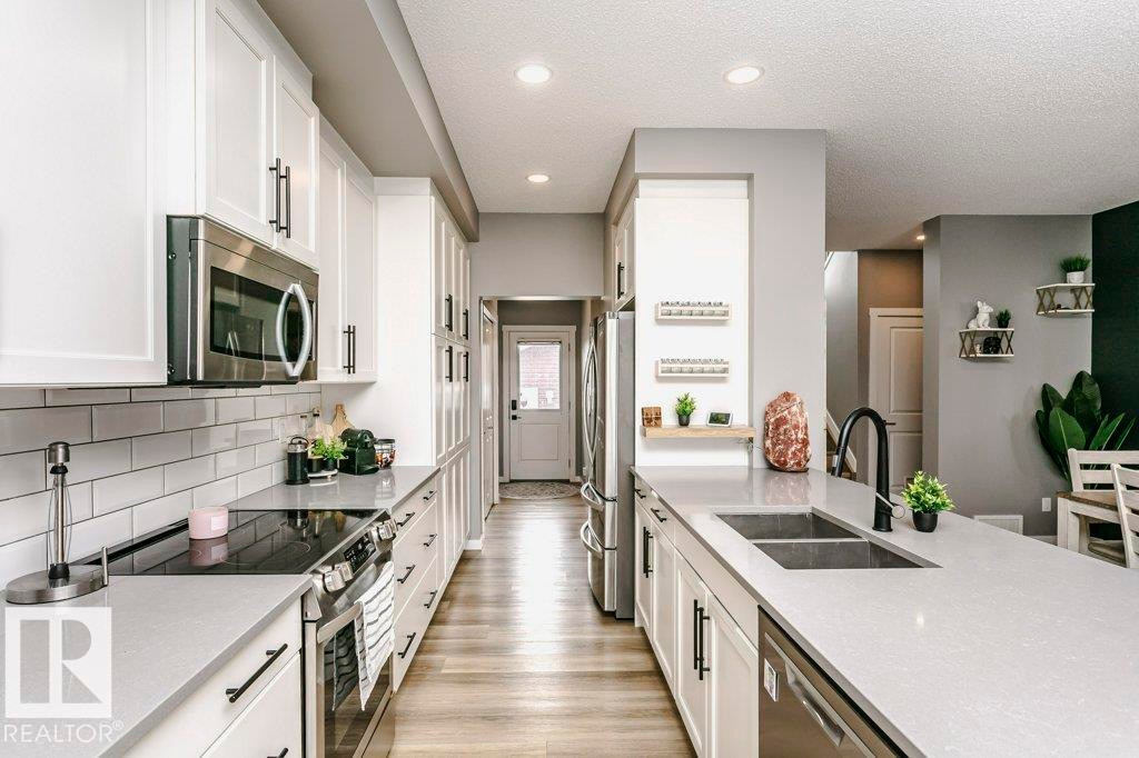 The kitchen features white cabinetry with black hardware, light-colored countertops, and stainless steel appliances including an oven, microwave, and dishwasher - 320 Balsam Link, Leduc, AB - Indoor Photo Showing Kitchen With Double Sink With Upgraded Kitchen