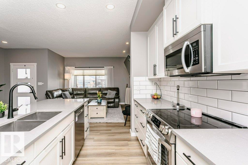 The kitchen features white cabinetry, a double basin sink with a matte black faucet, and stainless steel appliances - 320 Balsam Link, Leduc, AB - Indoor Photo Showing Kitchen With Double Sink With Upgraded Kitchen