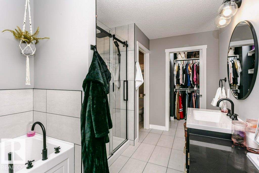 The bathroom features a standalone tub with a matte black faucet, a glass-enclosed shower, a vanity with a white rectangular sink, and an oval mirror - 320 Balsam Link, Leduc, AB - Indoor Photo Showing Bathroom