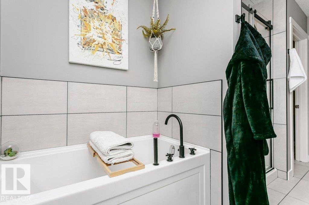 Bathroom featuring a white bathtub with a black faucet, and light-colored tiled walls - 320 Balsam Link, Leduc, AB - Indoor Photo Showing Bathroom
