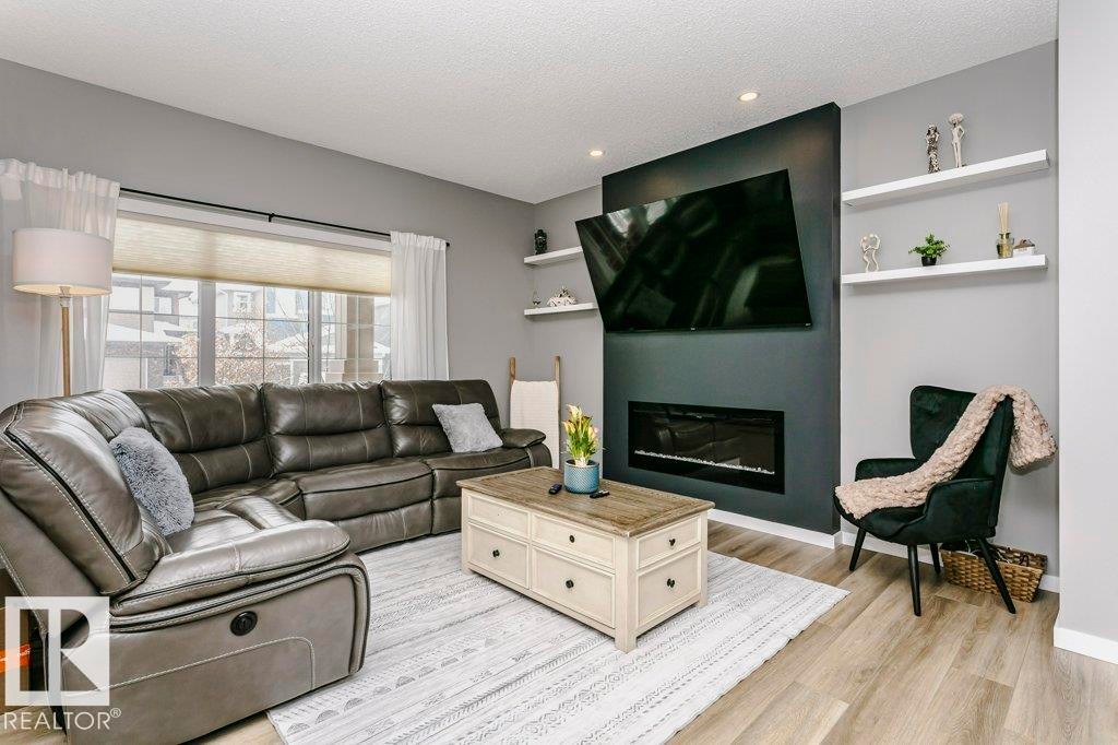 Living area featuring light wood flooring, a fireplace, and large windows with window coverings - 320 Balsam Link, Leduc, AB - Indoor Photo Showing Living Room With Fireplace