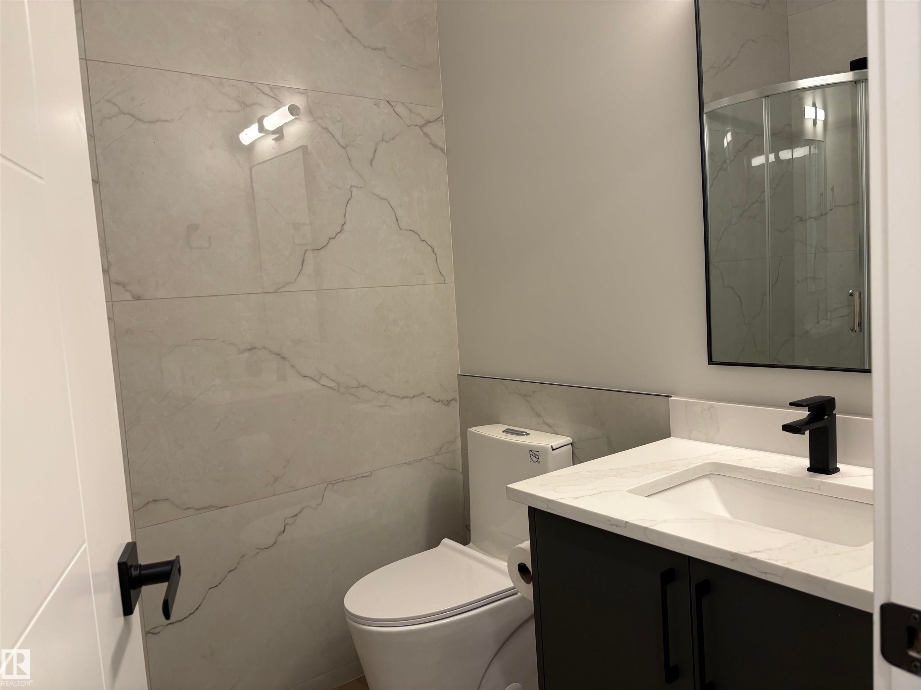 Contemporary bathroom featuring a dark vanity with a white countertop and integrated sink, matte black faucet, rectangular mirror, and light-toned, large-format tile walls - 1039 151 Ave, Edmonton, AB