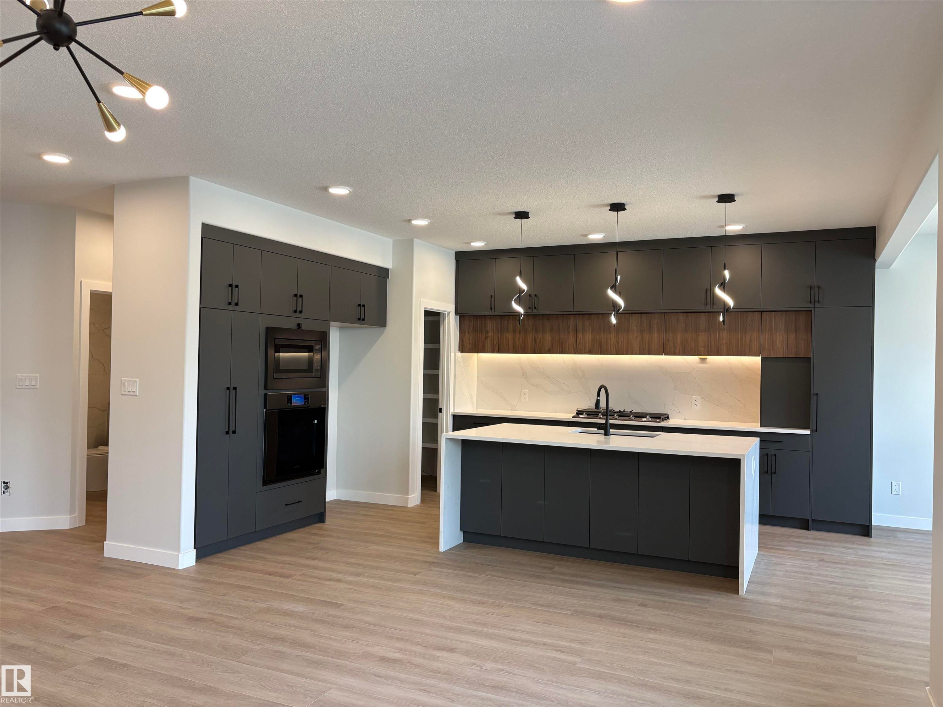 Modern kitchen featuring dark cabinetry, a spacious island with a white countertop, and integrated appliances - 1039 151 Ave, Edmonton, AB