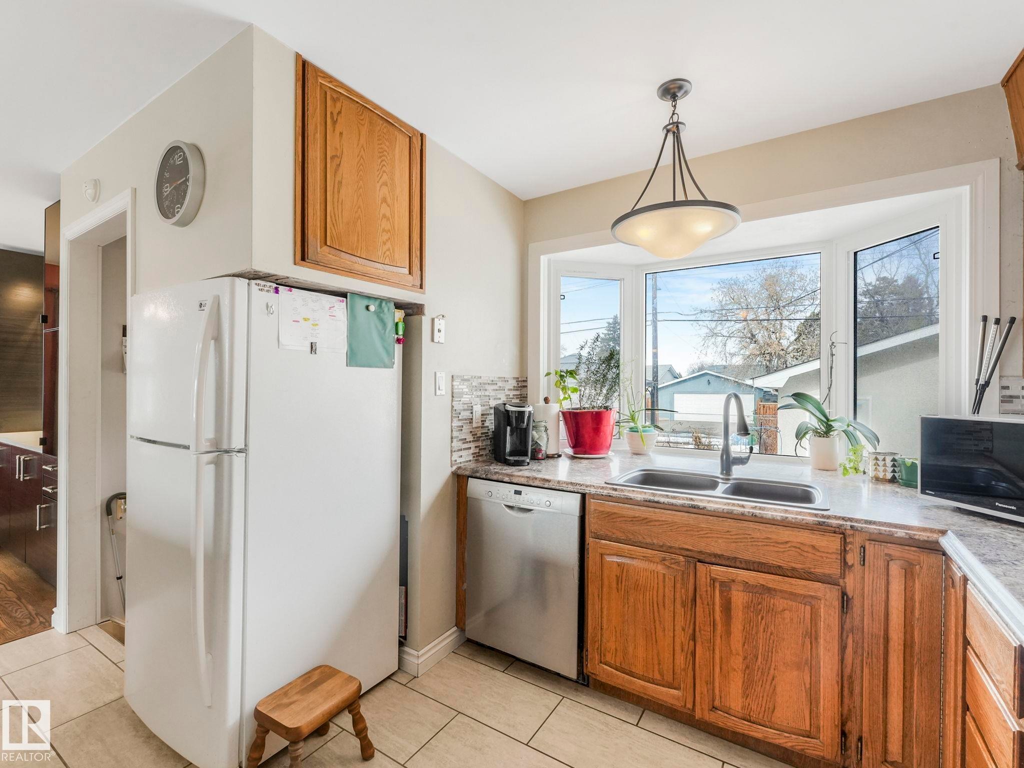 The kitchen features a large bay window, a stainless steel dishwasher, a double basin sink with a gooseneck faucet, and ample cabinetry - 16106 79A Avenue Nw, Edmonton, AB - Indoor Photo Showing Kitchen With Double Sink