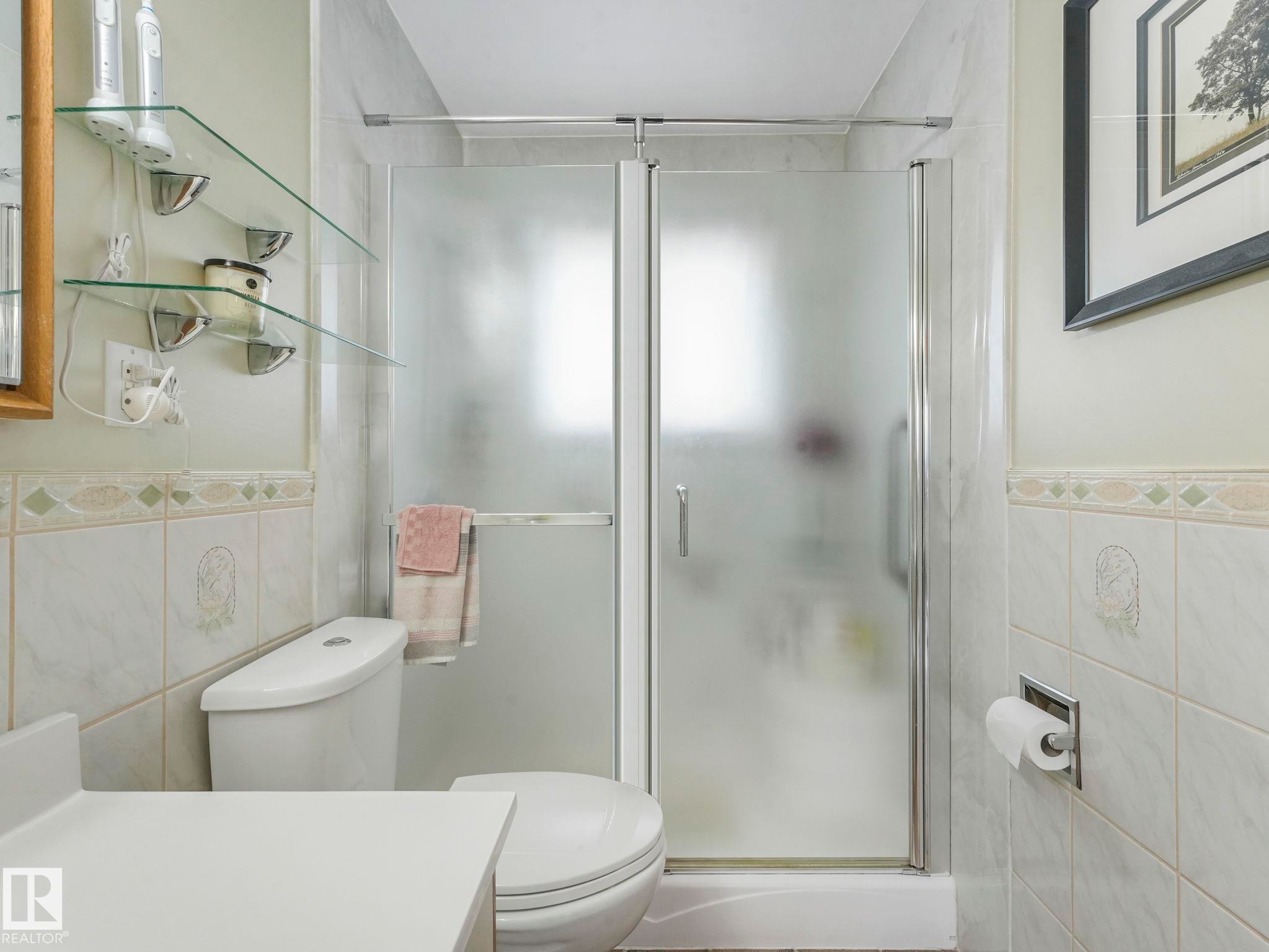 The bathroom features a toilet, a shower with frosted glass doors, and tiled walls - 16106 79A Avenue Nw, Edmonton, AB - Indoor Photo Showing Bathroom