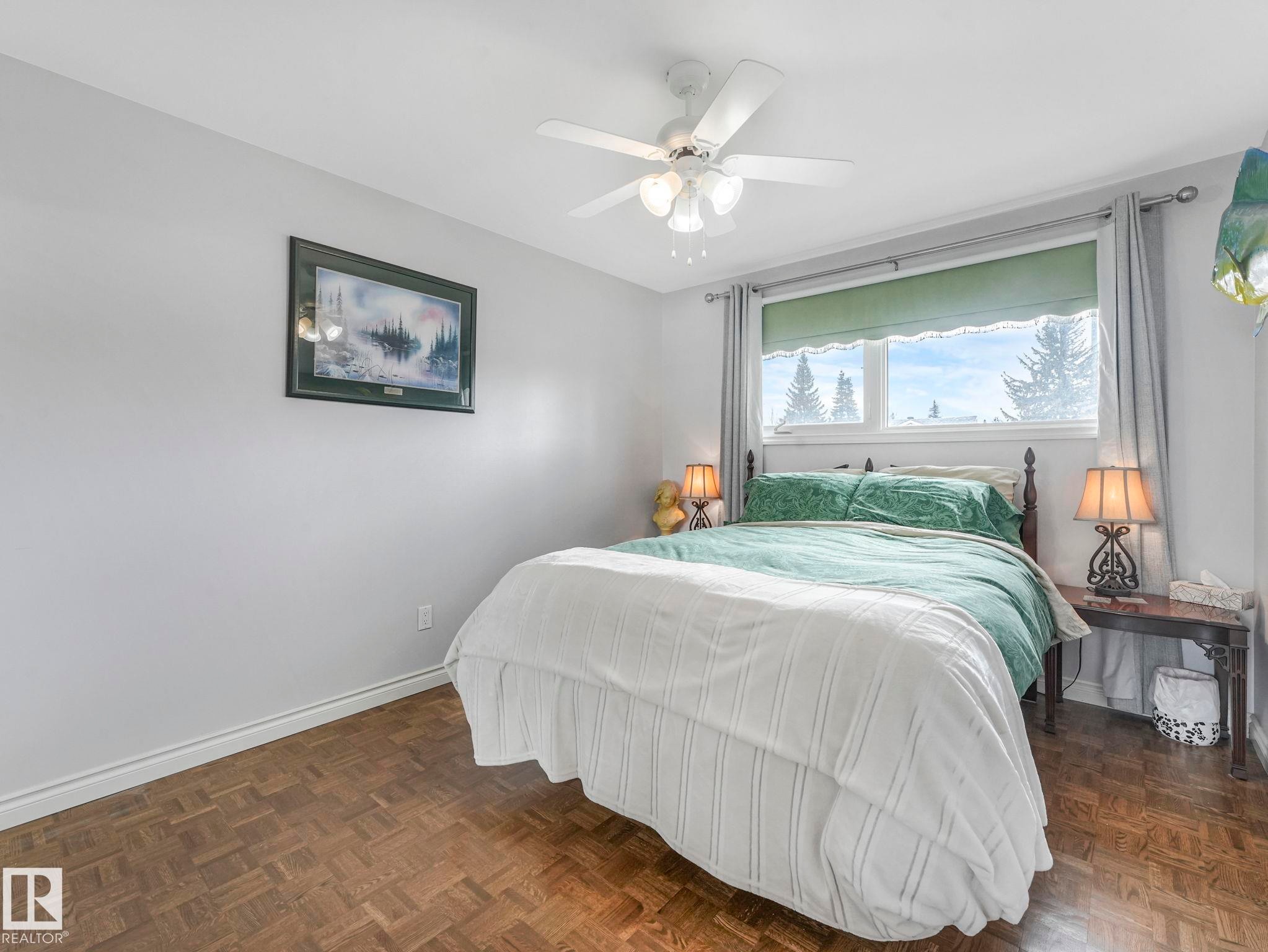 This inviting room features wood parquet flooring, a ceiling fan with integrated lighting, and a window with a green blind and curtains - 16106 79A Avenue Nw, Edmonton, AB - Indoor Photo Showing Bedroom