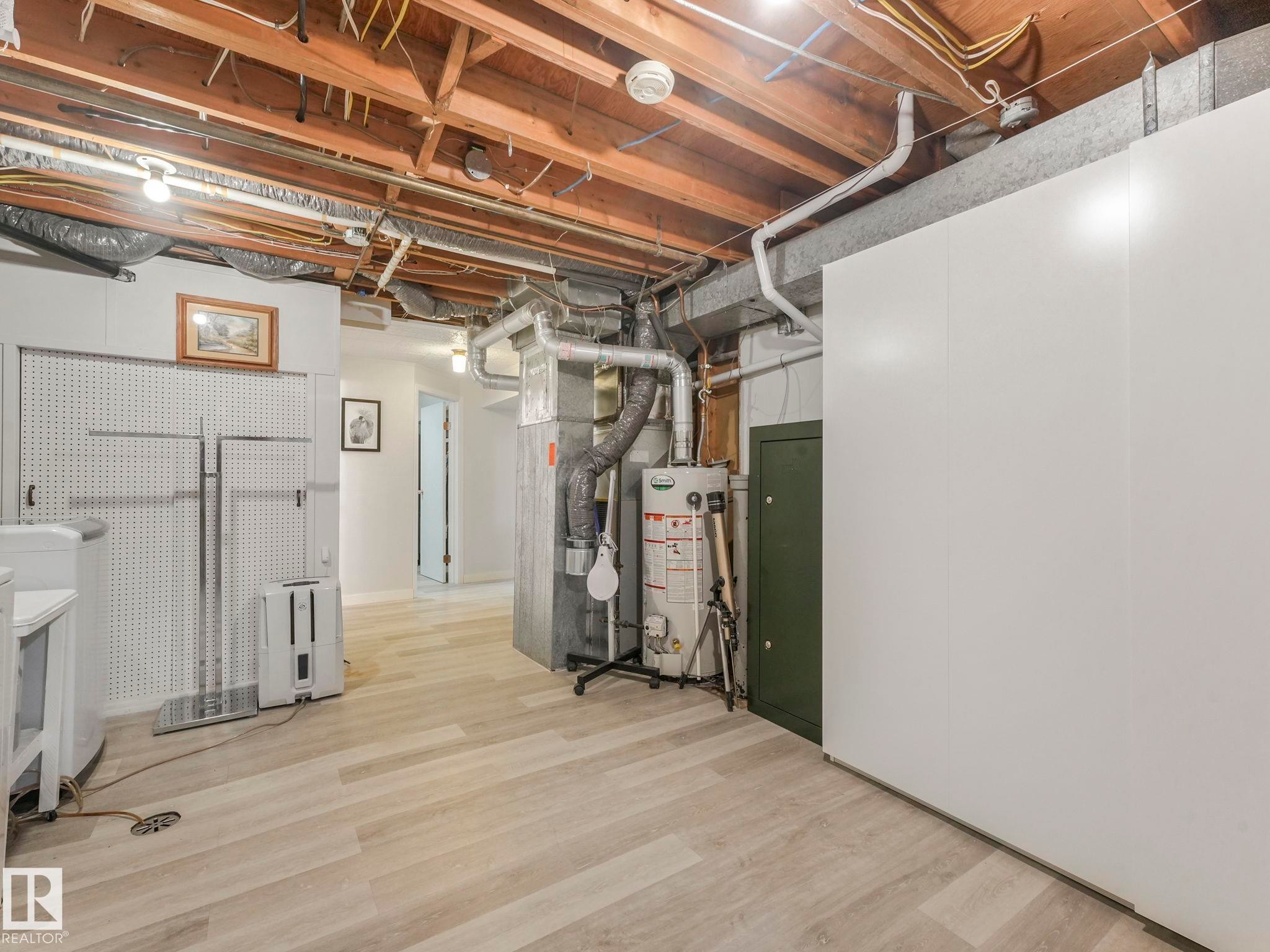 This space features light-colored flooring, exposed ceiling joists, and a hot water heater - 16106 79A Avenue Nw, Edmonton, AB - Indoor Photo Showing Basement