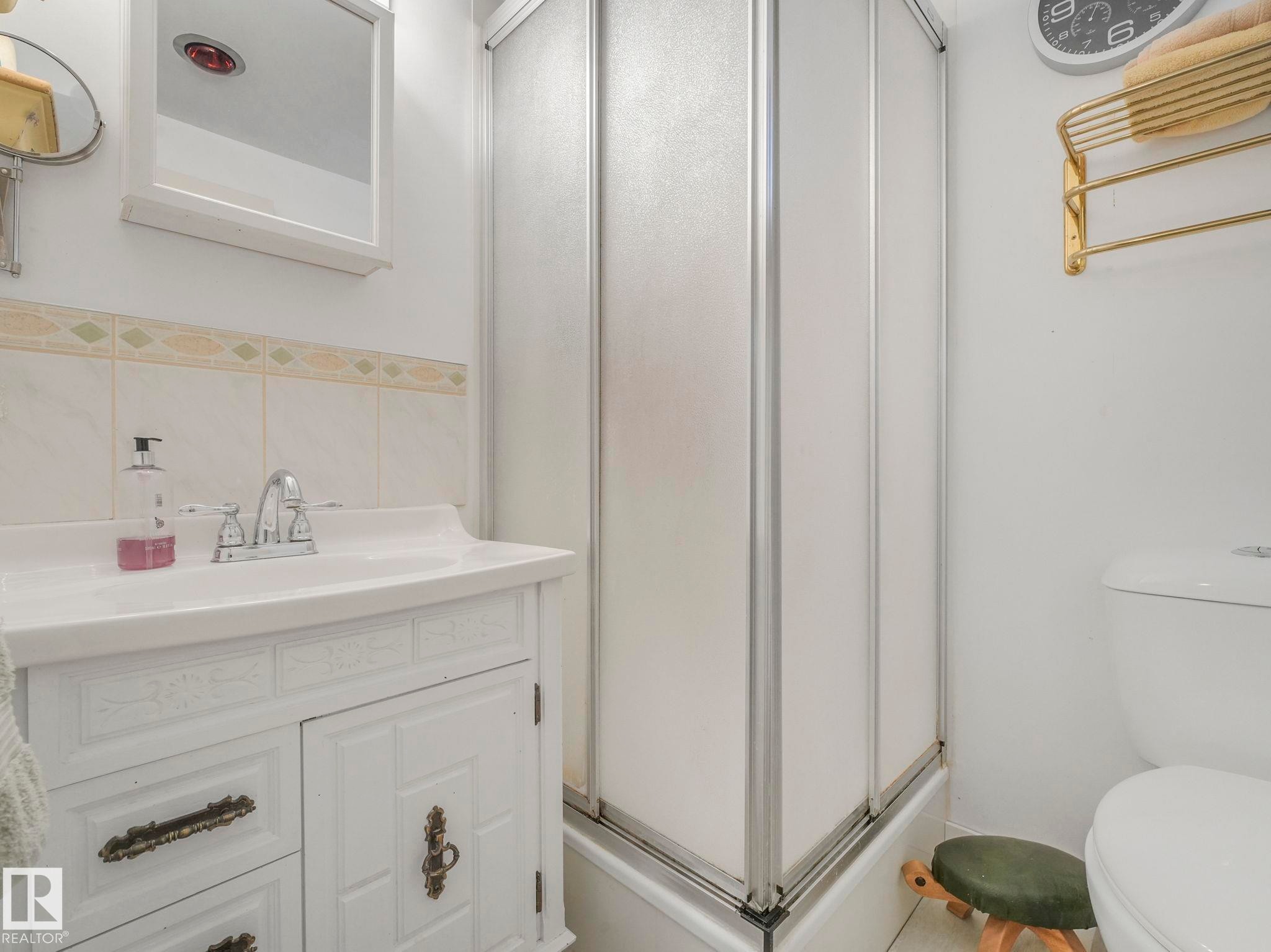 This bathroom features a shower enclosure with frosted panels, a white vanity with decorative hardware, and a white toilet - 16106 79A Avenue Nw, Edmonton, AB - Indoor Photo Showing Bathroom