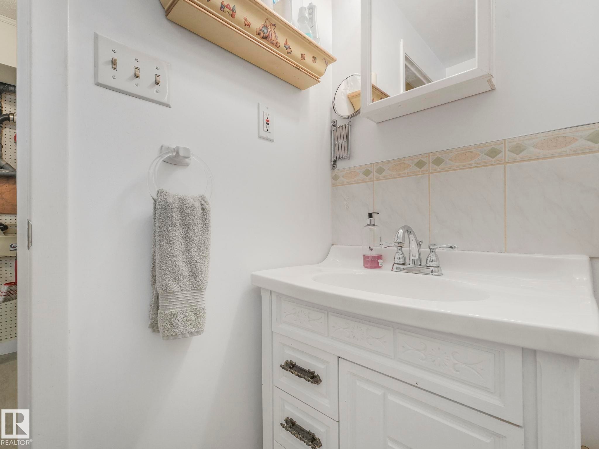 Bathroom vanity with a white integrated sink, chrome faucet, and tiled backsplash - 16106 79A Avenue Nw, Edmonton, AB - Indoor Photo Showing Bathroom