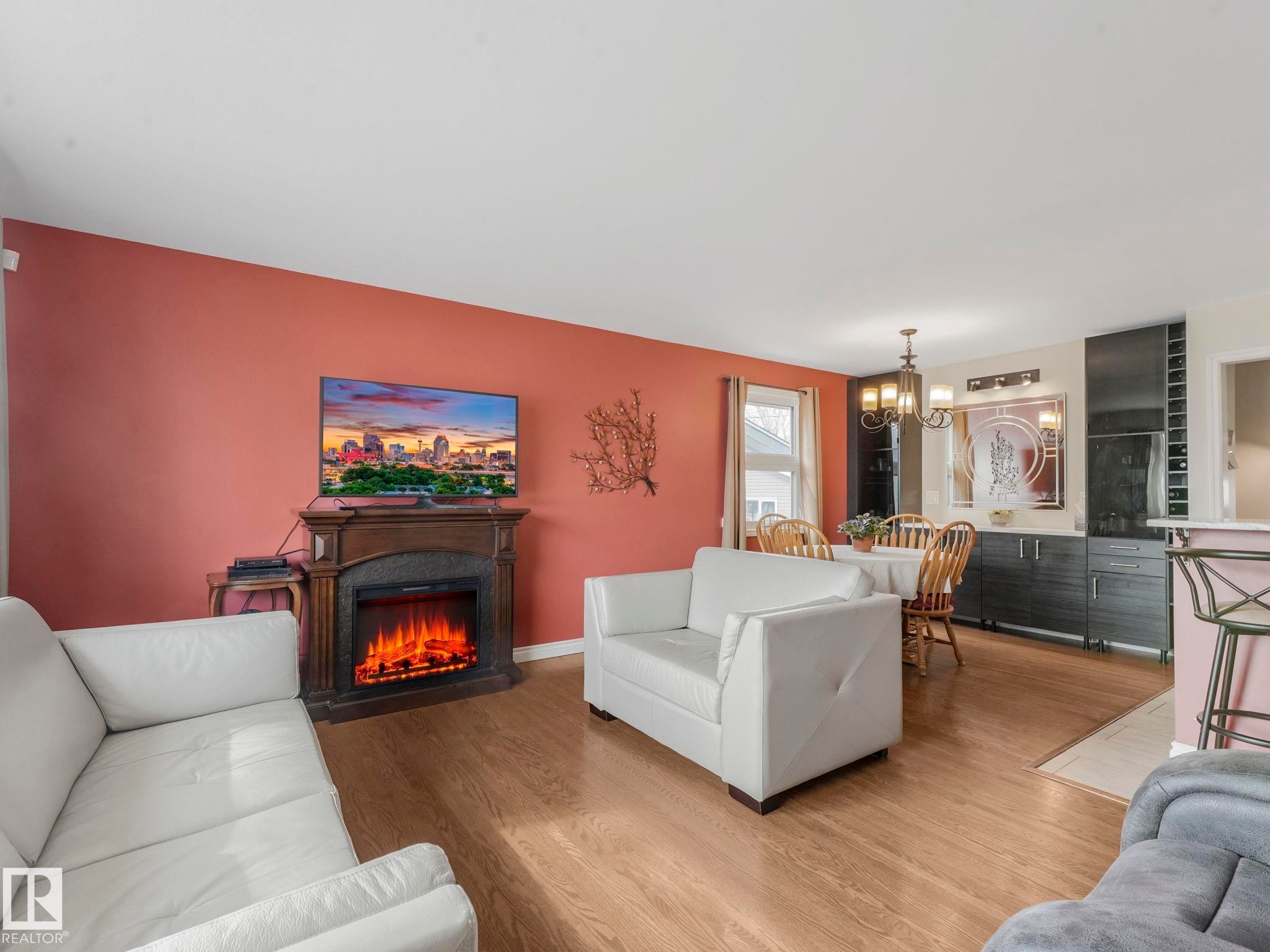 Living area featuring light wood flooring, a fireplace with a decorative mantel, and a dining area with a chandelier - 16106 79A Avenue Nw, Edmonton, AB - Indoor Photo Showing Living Room With Fireplace