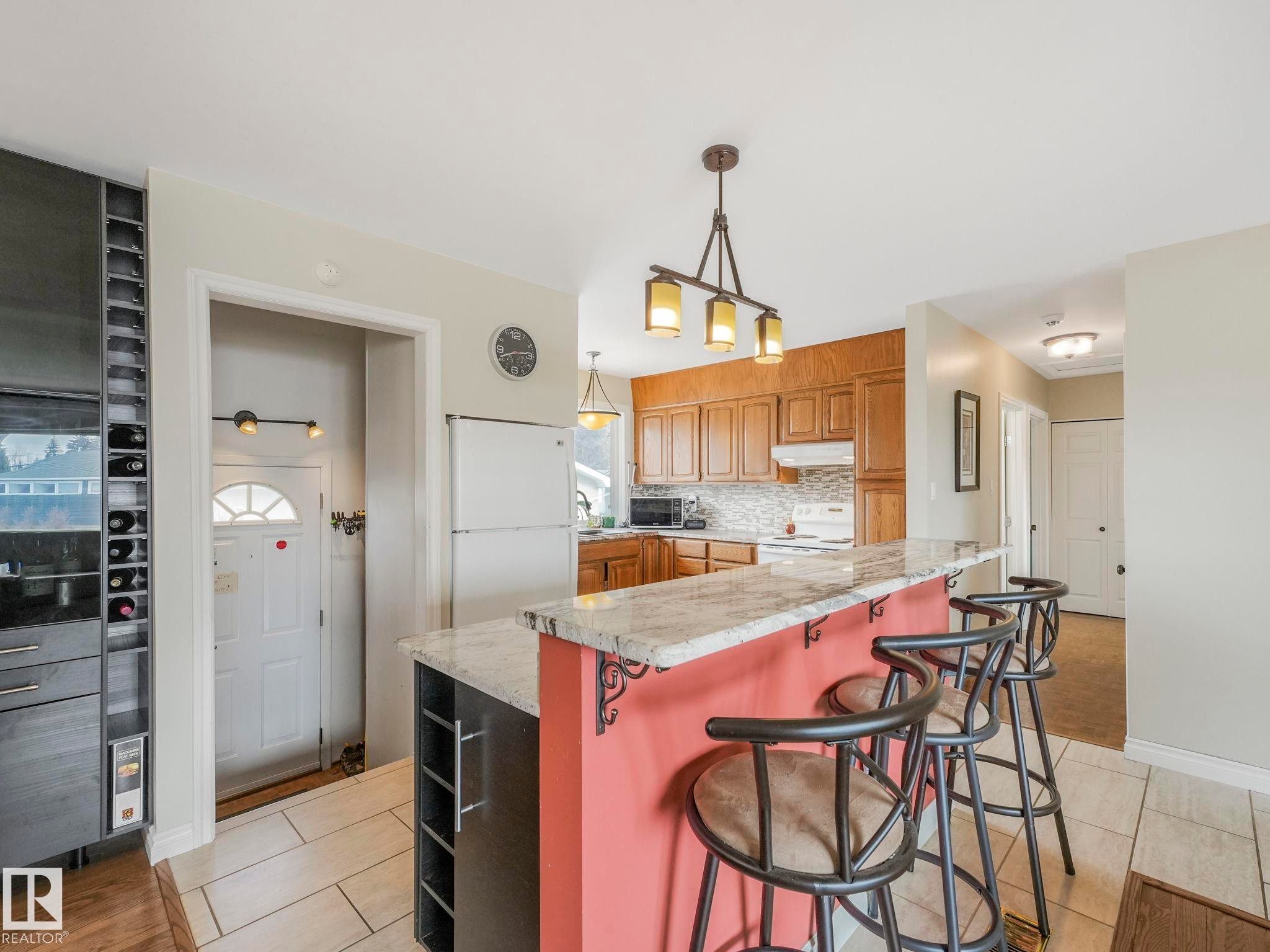Kitchen featuring a breakfast bar with a granite countertop and seating for three, wood cabinetry, and a tile backsplash - 16106 79A Avenue Nw, Edmonton, AB - Indoor Photo Showing Kitchen