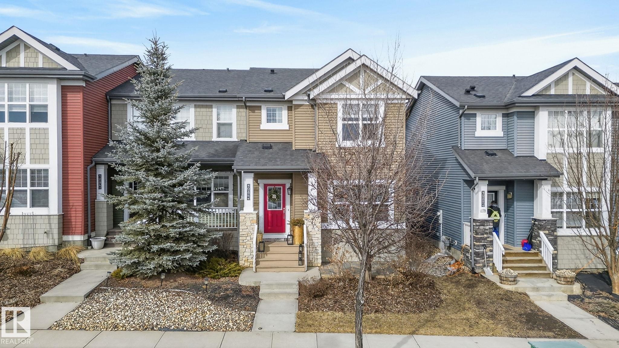 The property features a red front door, a front porch with white railings, and stone accent pillars - 9084 Rosenthal Link, Edmonton, AB - Outdoor With Facade