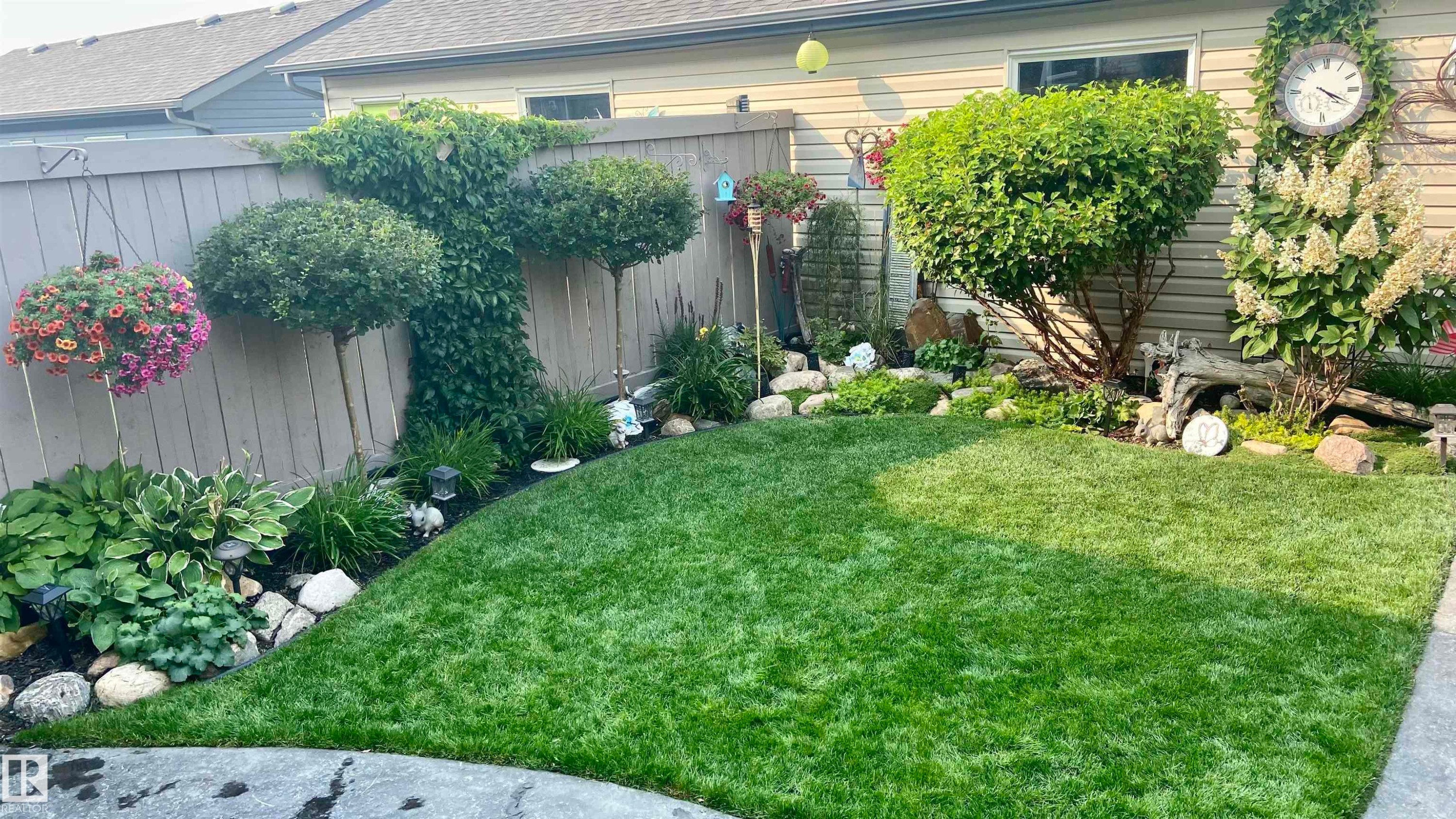 The property features a meticulously maintained lawn, bordered by a decorative rock garden with diverse plant species, including hostas and topiary trees - 2914 18A Avenue, Edmonton, AB - Outdoor
