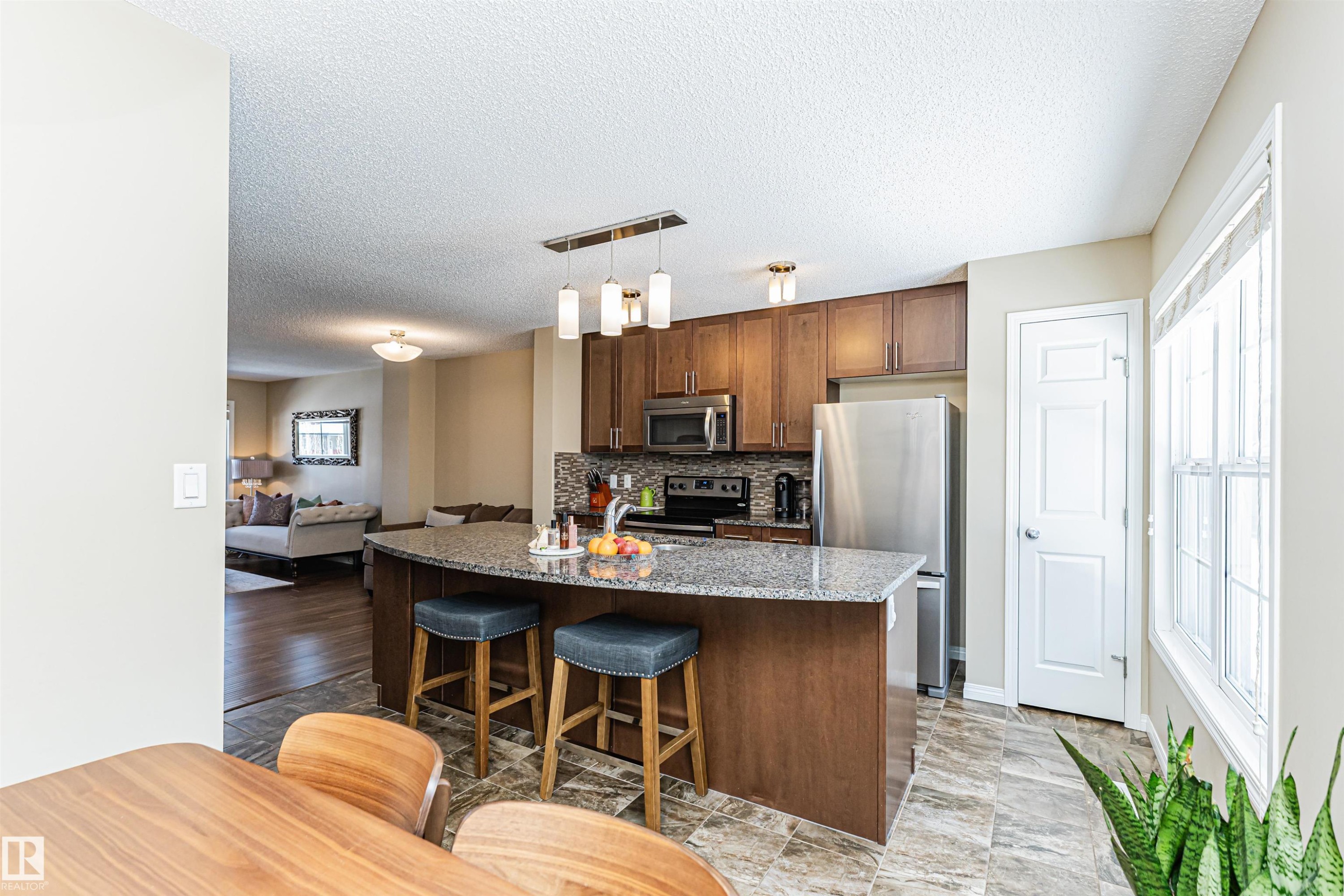 The kitchen features wood cabinetry, stainless steel appliances, a tiled backsplash, and a granite island with seating - 31 4029 Orchards Drive, Edmonton, autreother - Indoor Photo Showing Kitchen