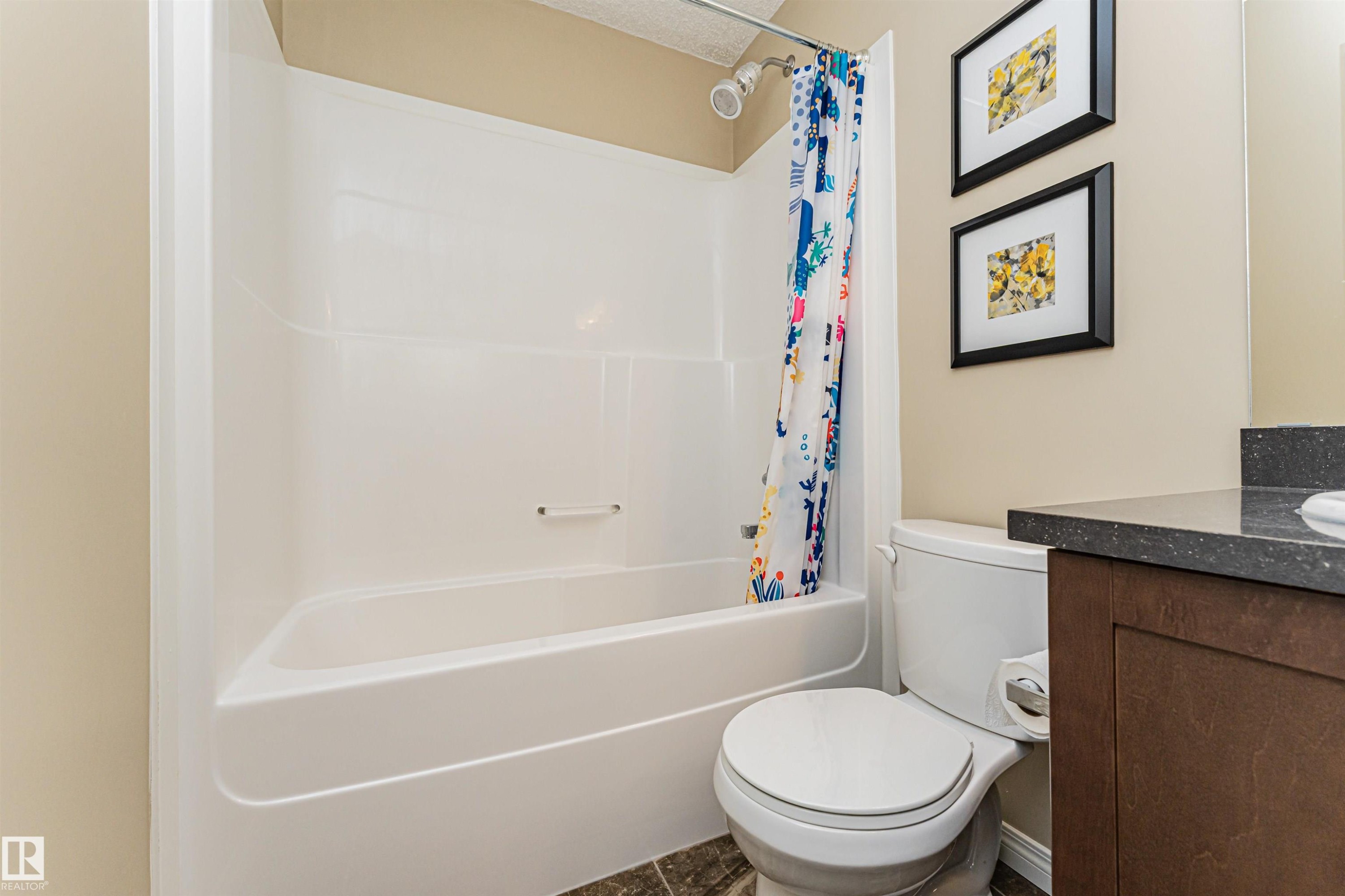 Bathroom featuring a white shower and bathtub combination unit, a toilet, and a vanity with a dark countertop - 31 4029 Orchards Drive, Edmonton, autreother - Indoor Photo Showing Bathroom