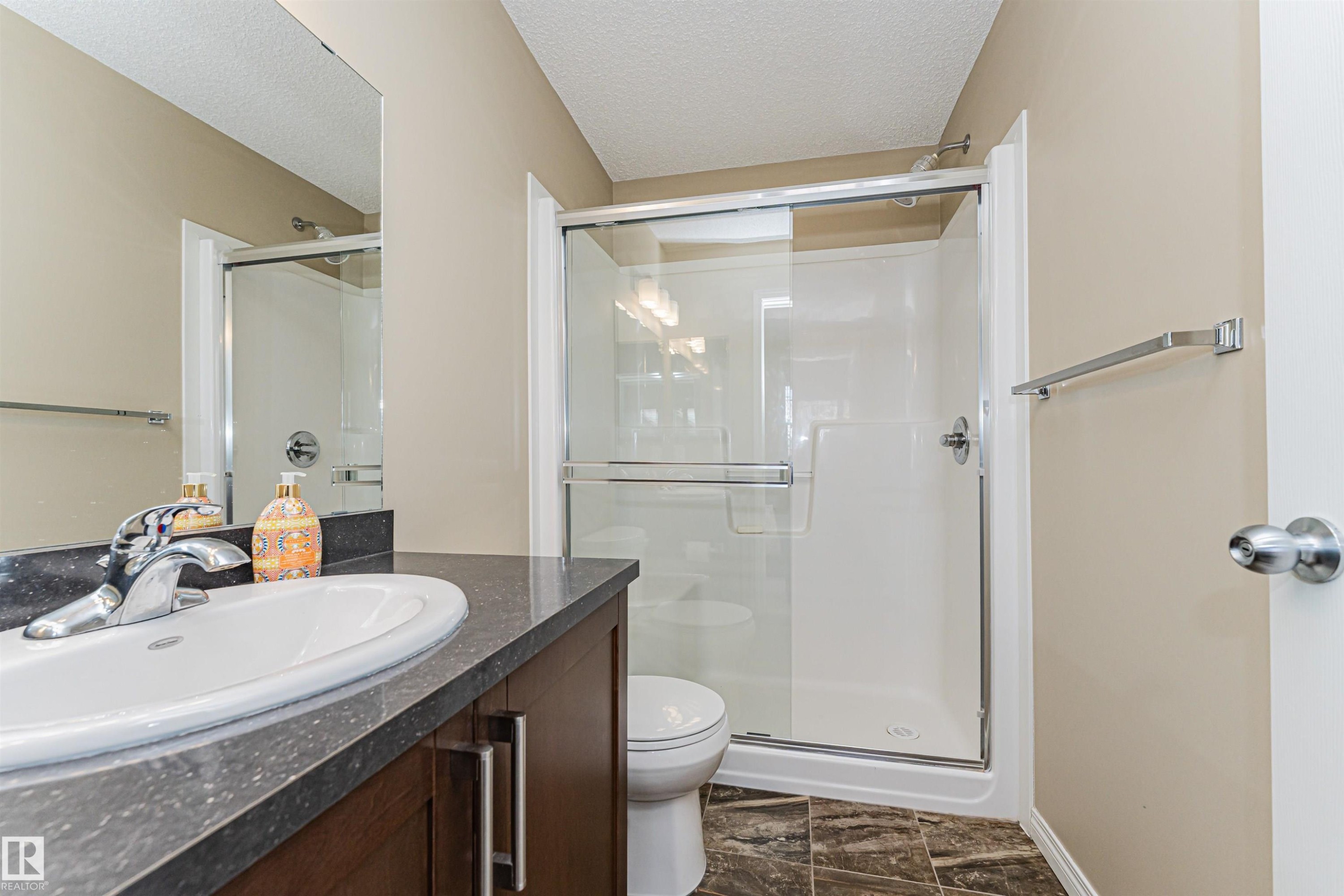 Bathroom featuring a vanity with a white oval sink and dark countertop, a walk-in shower with a glass enclosure, and dark tiled flooring - 31 4029 Orchards Drive, Edmonton, autreother - Indoor Photo Showing Bathroom