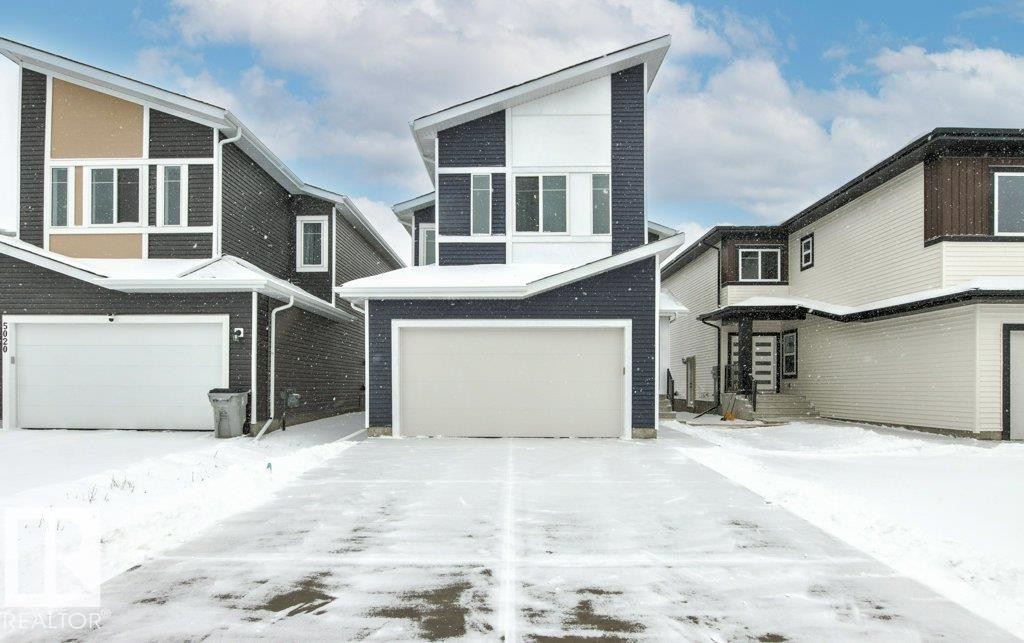 Contemporary property with a striking dark blue and white exterior, featuring a prominent white garage door and an angled roofline - 5018 53 Avenue, Calmar, AB - Outdoor With Facade