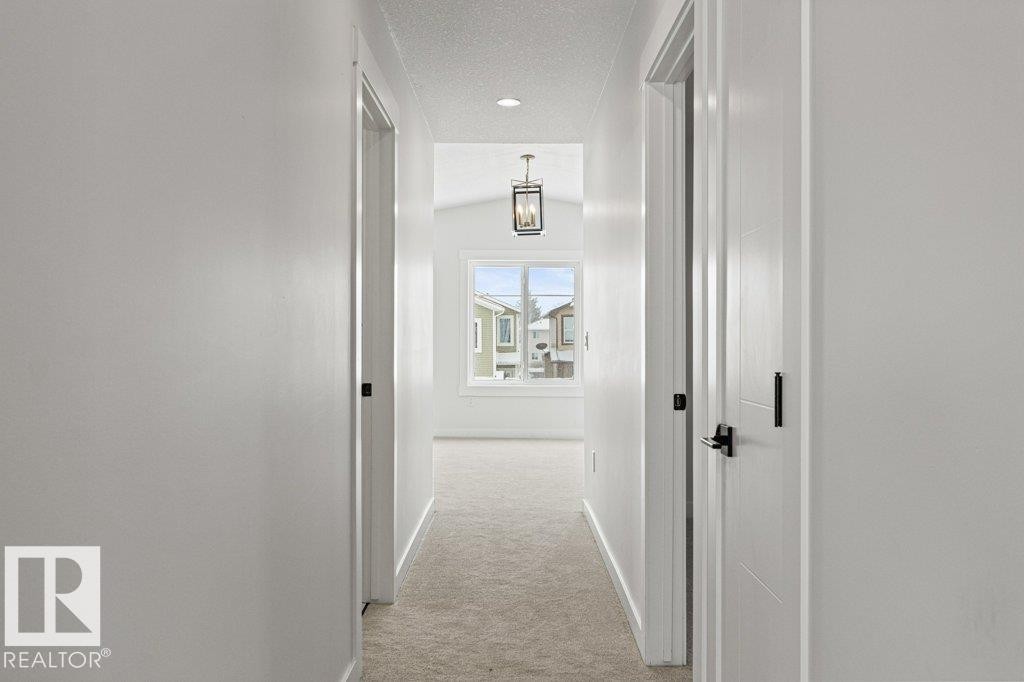 Hallway with light-colored walls and carpeting, featuring several doors with dark hardware, and a window providing natural light at the far end - 5018 53 Avenue, Calmar, AB - Indoor Photo Showing Other Room