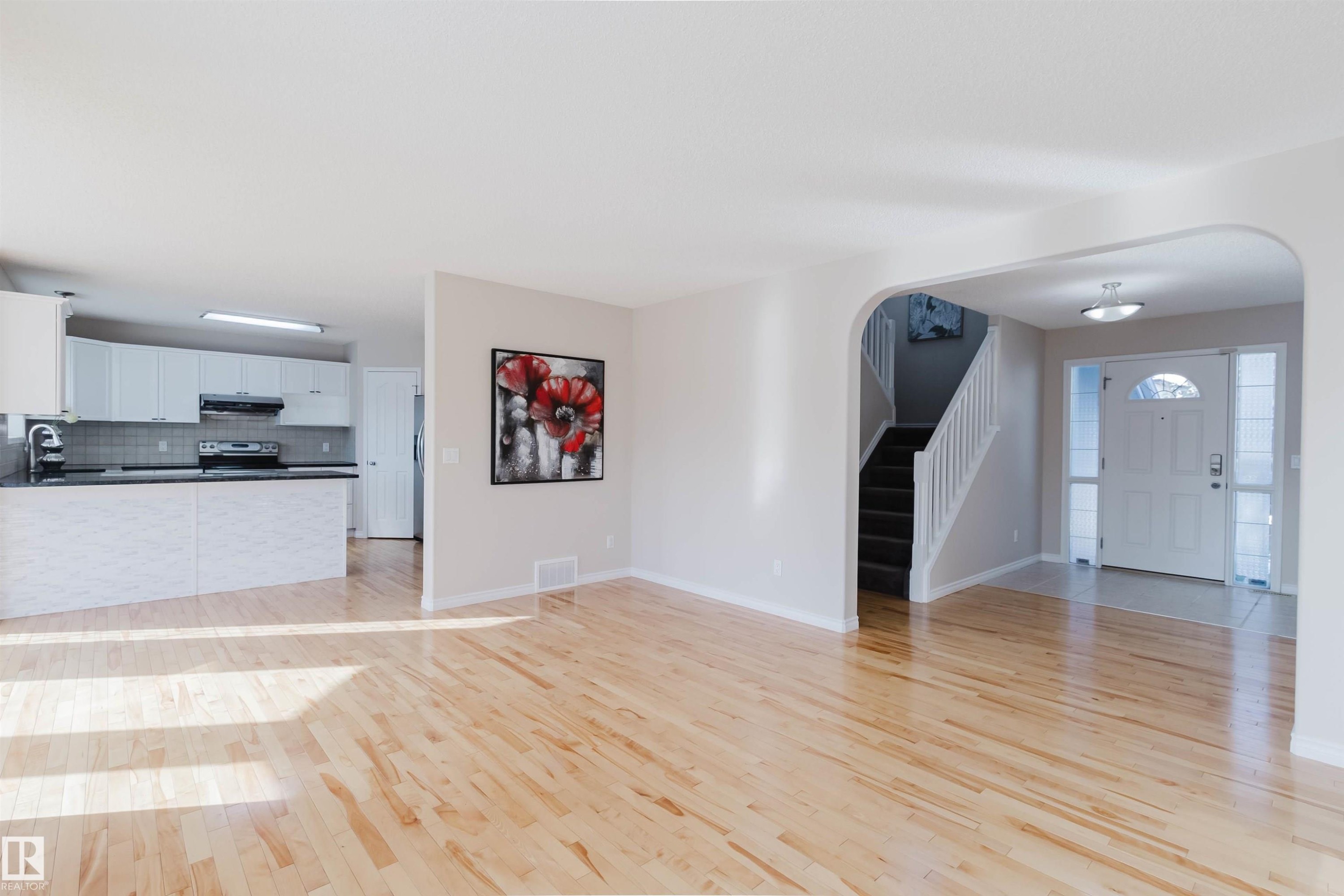 Open concept living area featuring light hardwood flooring, light-colored walls, and a view of the kitchen with white cabinetry and dark countertops - 1135 112 Street, Edmonton, AB - Indoor Photo Showing Kitchen