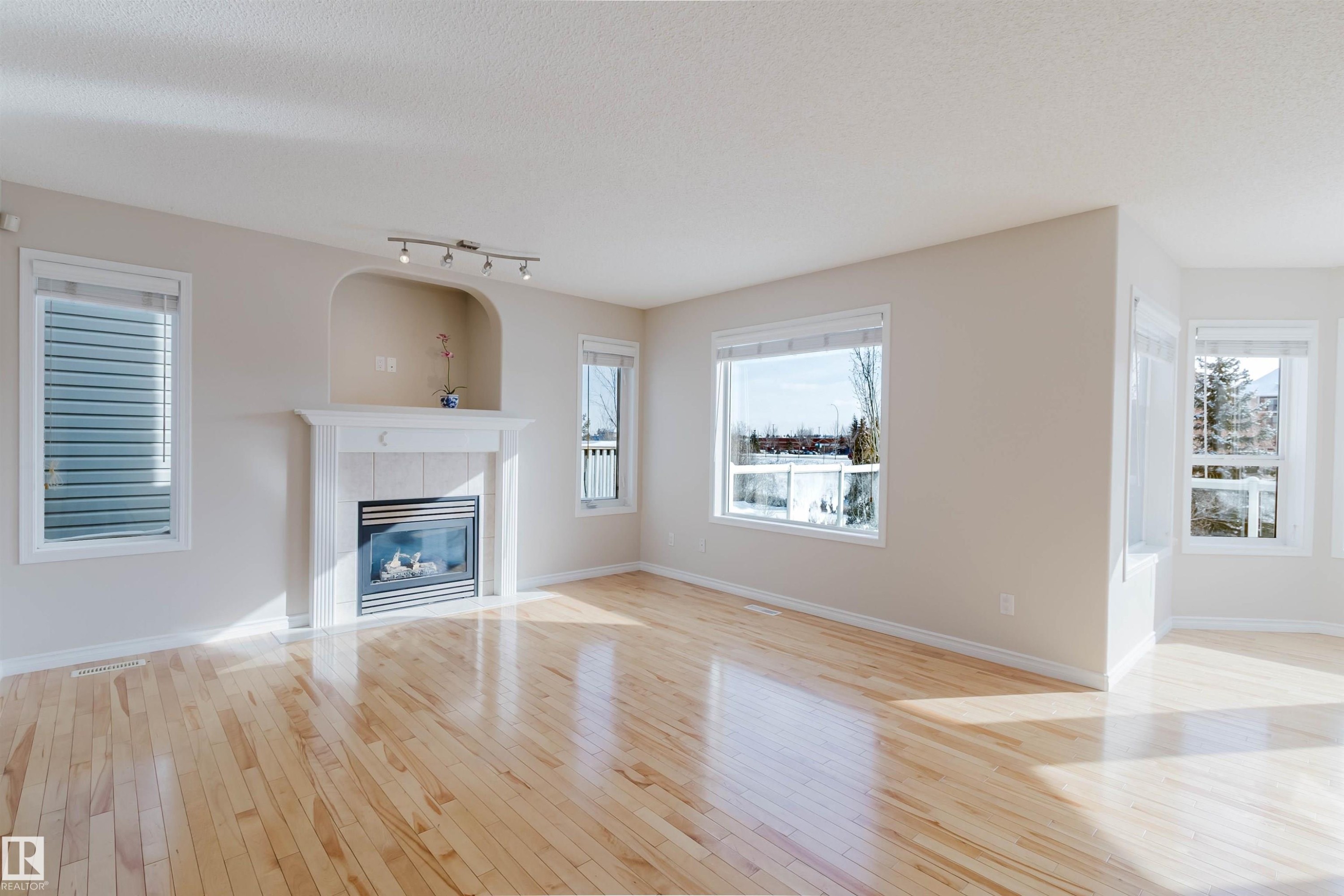 The property features hardwood floors, a fireplace with a stone hearth and mantel, and large windows offering exterior views - 1135 112 Street, Edmonton, AB - Indoor Photo Showing Living Room With Fireplace