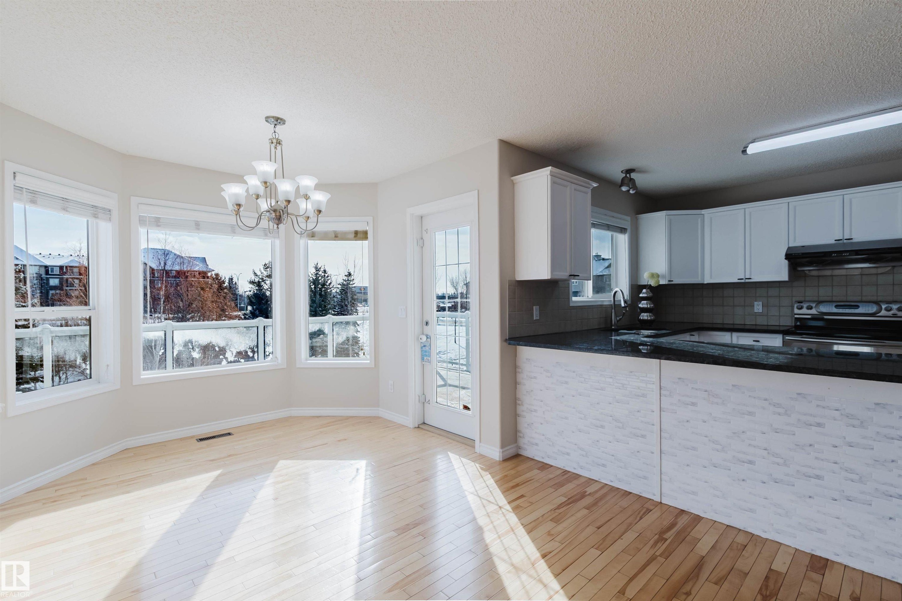 The property features an open-concept layout with light wood flooring and a kitchen featuring white cabinetry, dark countertops, and a black oven - 1135 112 Street, Edmonton, AB - Indoor Photo Showing Kitchen With Double Sink