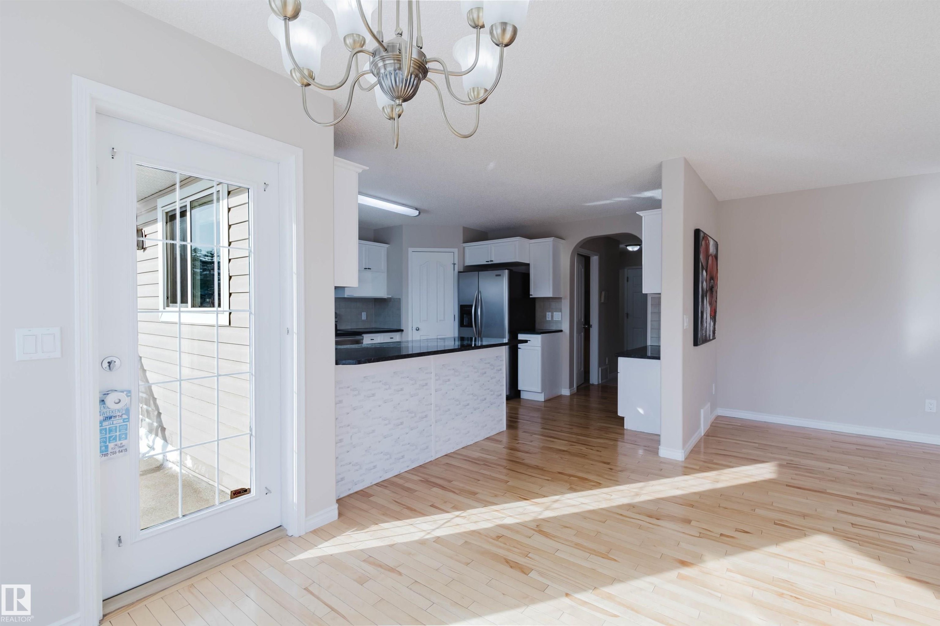 The property features light-colored hardwood flooring, a white glass-paneled door, and a kitchen with white cabinetry and dark countertops - 1135 112 Street, Edmonton, AB - Indoor Photo Showing Kitchen