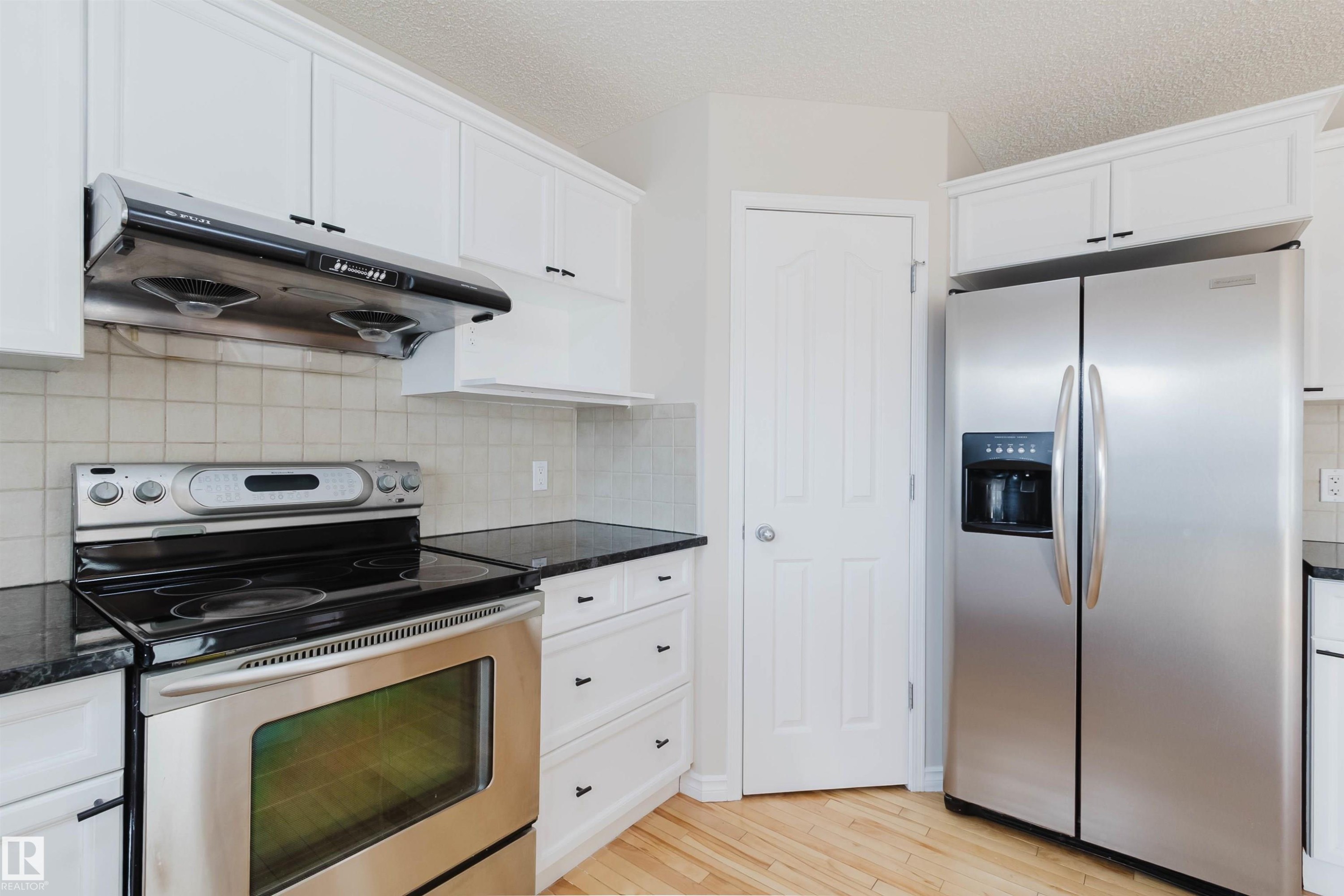 The kitchen features white cabinetry, dark countertops, and stainless steel appliances, including a range and a side-by-side refrigerator - 1135 112 Street, Edmonton, AB - Indoor Photo Showing Kitchen