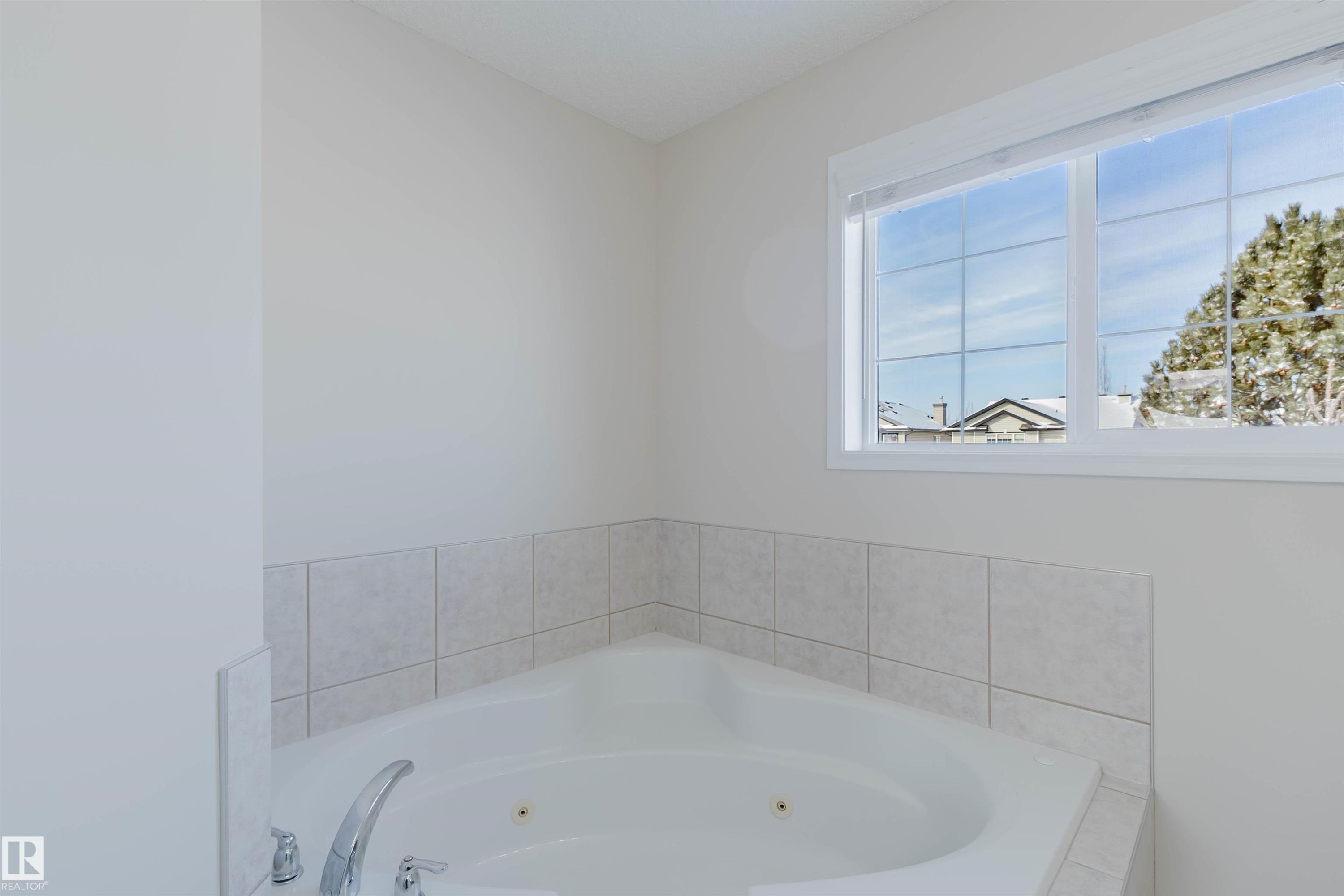 Corner bathtub featuring a tiled surround, chrome fixtures, and a window providing natural light - 1135 112 Street, Edmonton, AB - Indoor Photo Showing Bathroom