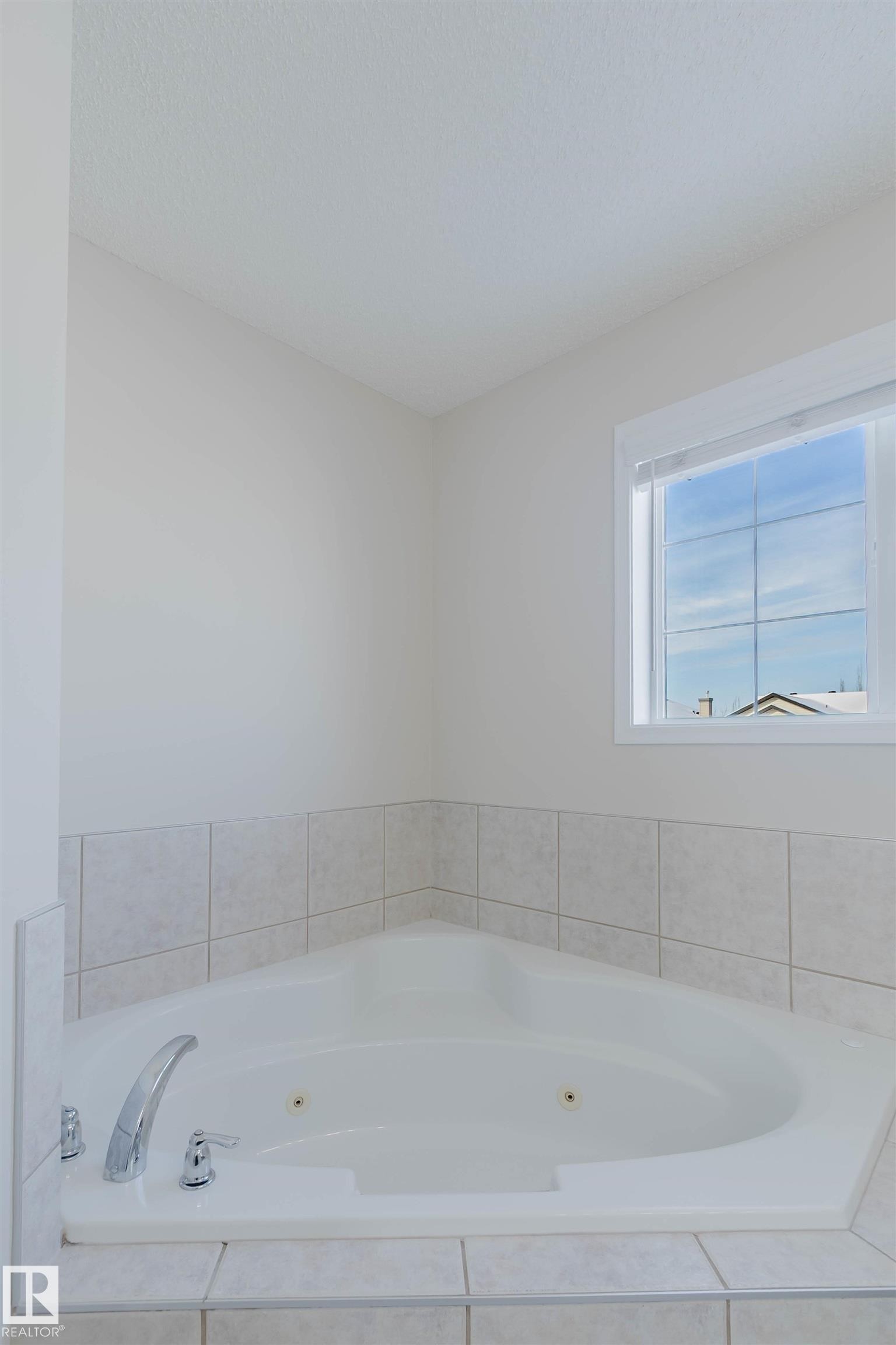 The property includes a corner bathtub with jets, surrounded by tiled walls, and features a window providing natural light - 1135 112 Street, Edmonton, AB - Indoor Photo Showing Bathroom