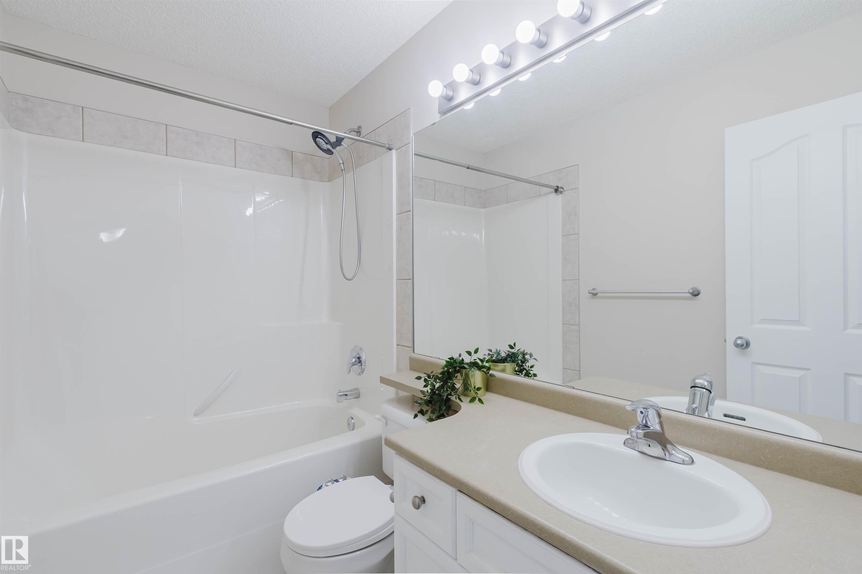 Bathroom featuring a white bathtub and shower with tiled surround, a vanity with a light-colored countertop and an integrated sink, and a large mirror with overhead lighting - 1135 112 Street, Edmonton, AB - Indoor Photo Showing Bathroom