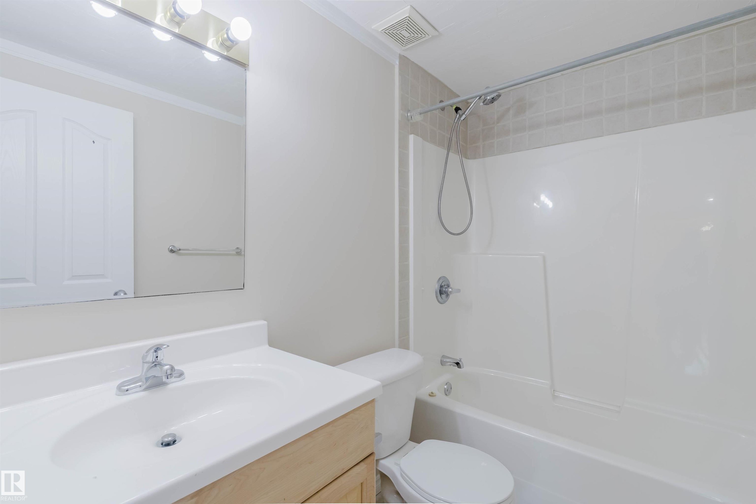 Bathroom featuring a vanity with an integrated sink and chrome faucet, a large mirror with overhead lighting, and a bathtub with a shower - 1135 112 Street, Edmonton, AB - Indoor Photo Showing Bathroom