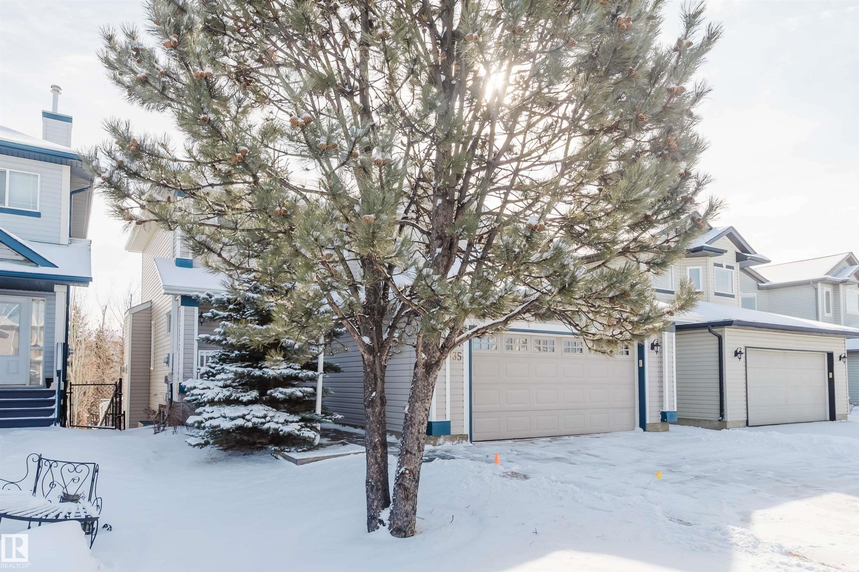 The property features light-colored siding, a front-facing garage, and a snow-covered yard with mature trees - 1135 112 Street, Edmonton, AB - Outdoor