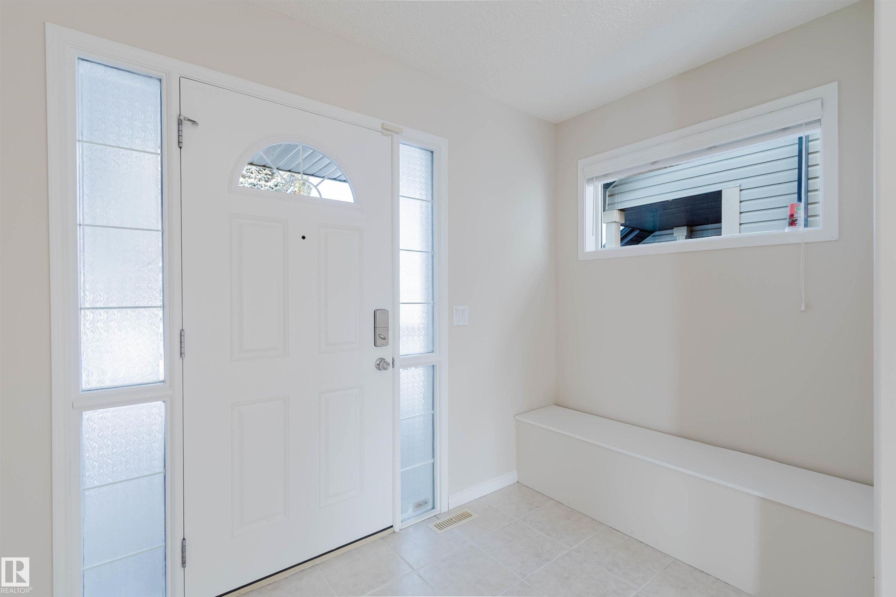 The entryway features a white front door with an arched window and two frosted glass sidelights, light-colored walls, and a built-in bench below a horizontal window - 1135 112 Street, Edmonton, AB - Indoor Photo Showing Other Room