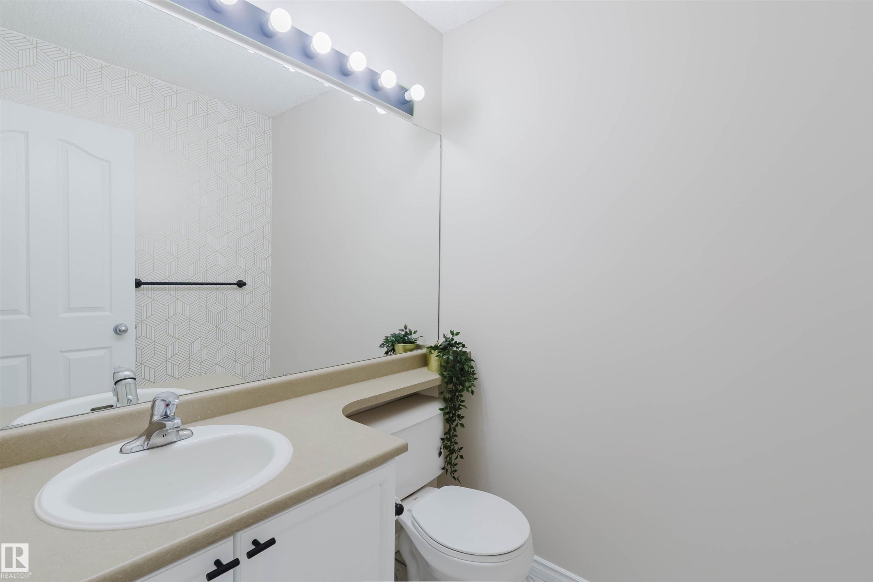 Bathroom featuring a vanity with a light-colored countertop and an integrated sink, a large mirror with overhead lighting, and a toilet - 1135 112 Street, Edmonton, AB - Indoor Photo Showing Bathroom