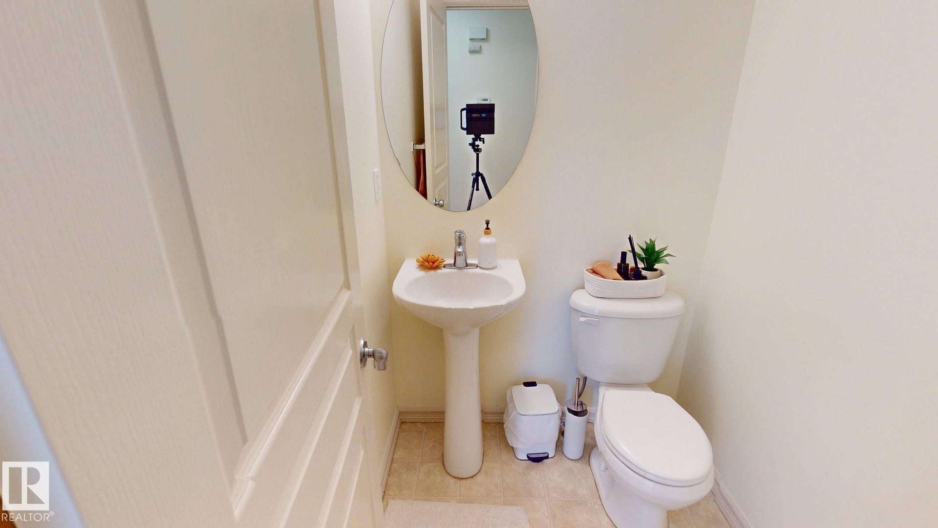 This powder room features a pedestal sink, an oval mirror, and light-colored walls - 1609 Hodgson Crest, Edmonton, AB - Indoor Photo Showing Bathroom
