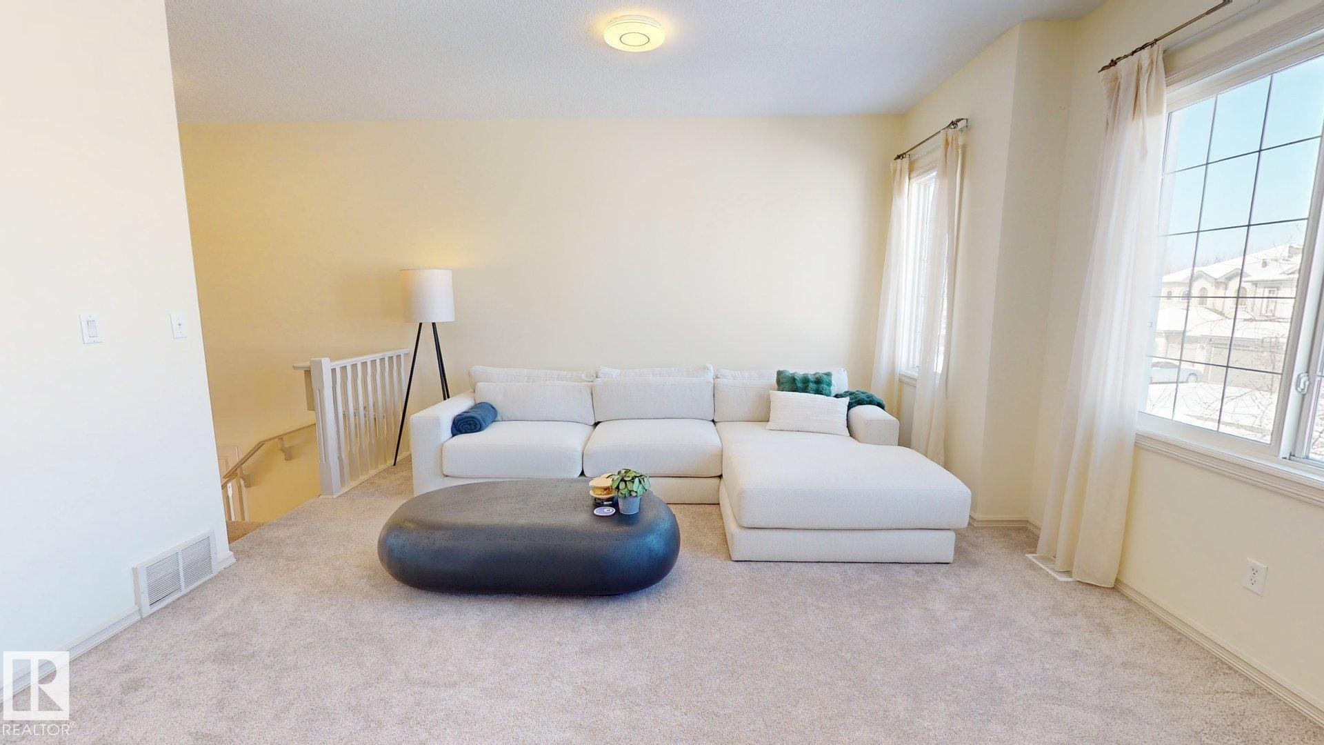 Living area featuring light-colored walls, carpeted floors, and a window with a view of other properties - 1609 Hodgson Crest, Edmonton, AB - Indoor