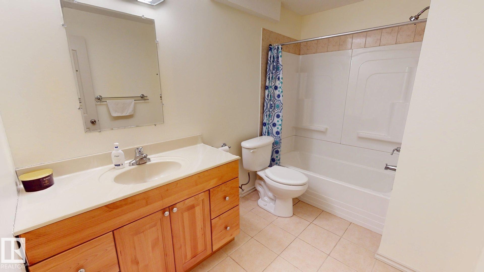 Full bathroom featuring a vanity with a light wood cabinet and light-colored countertop, a toilet, a bathtub with a shower, and tiled flooring - 1609 Hodgson Crest, Edmonton, AB - Indoor Photo Showing Bathroom