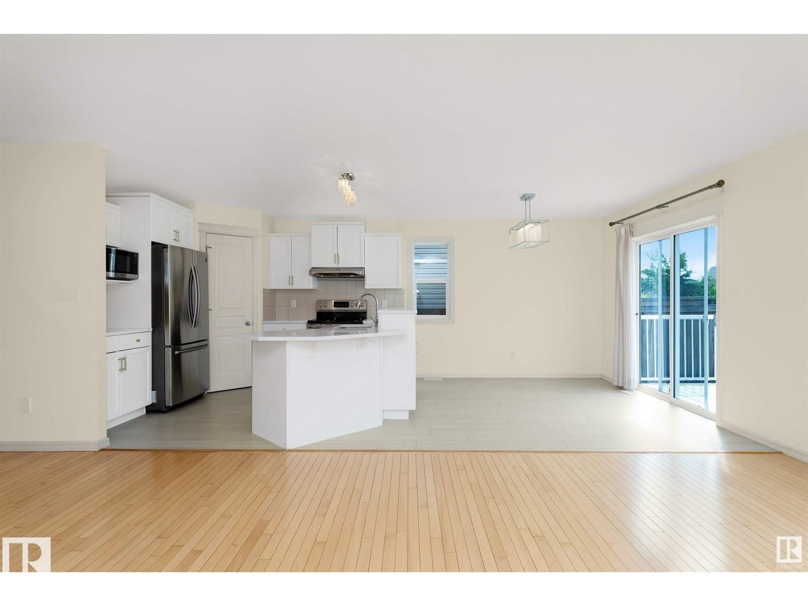 This property features light-colored hardwood flooring, a kitchen with white cabinetry and stainless steel appliances, and a sliding glass door leading to a balcony - 1609 Hodgson Crest, Edmonton, AB - Indoor Photo Showing Kitchen