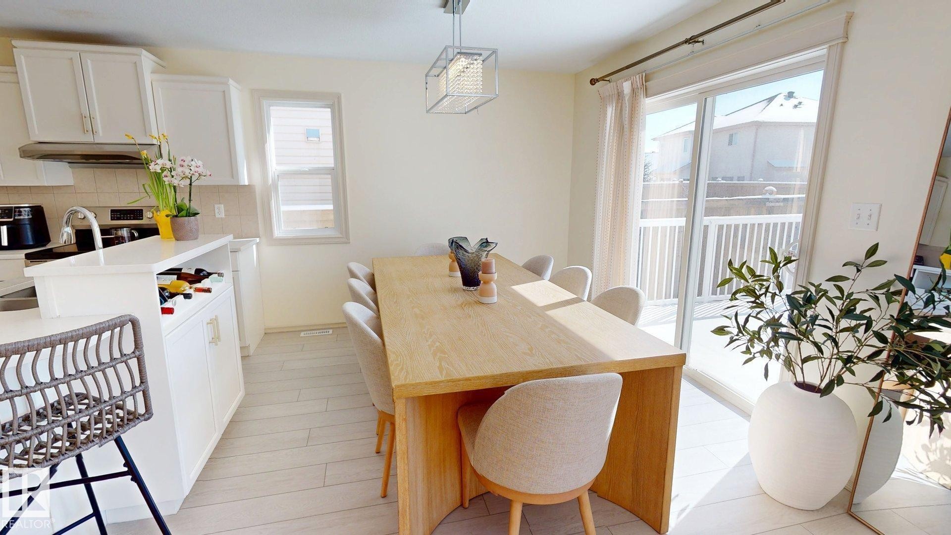 Bright dining area featuring a light wood table, upholstered chairs, and a contemporary light fixture, with sliding glass doors opening to an exterior deck - 1609 Hodgson Crest, Edmonton, AB - Indoor