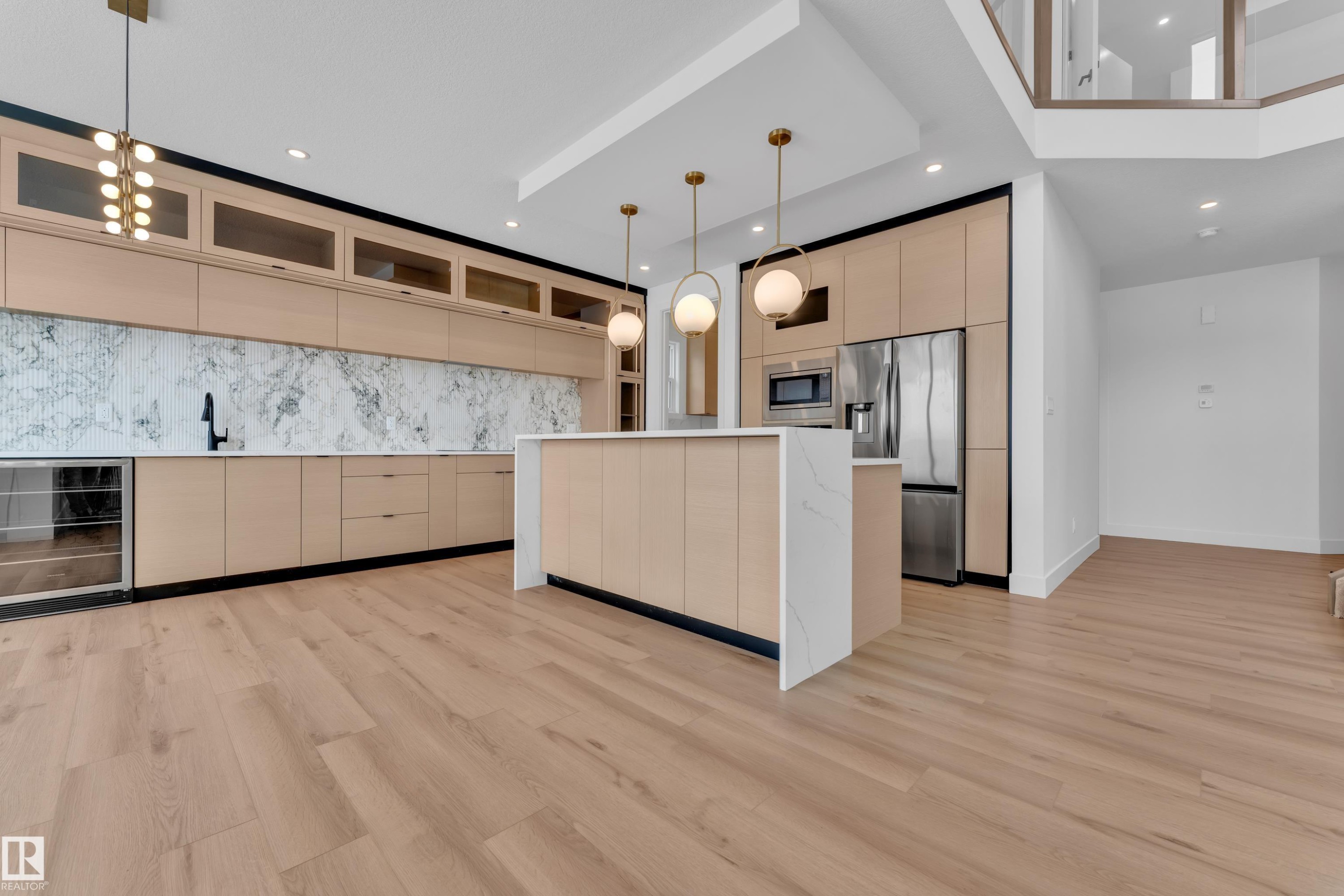 The kitchen features light wood cabinetry, a white marble backsplash, and a central island with a white countertop - 503 Creekside Bay, Leduc, AB - Indoor Photo Showing Kitchen