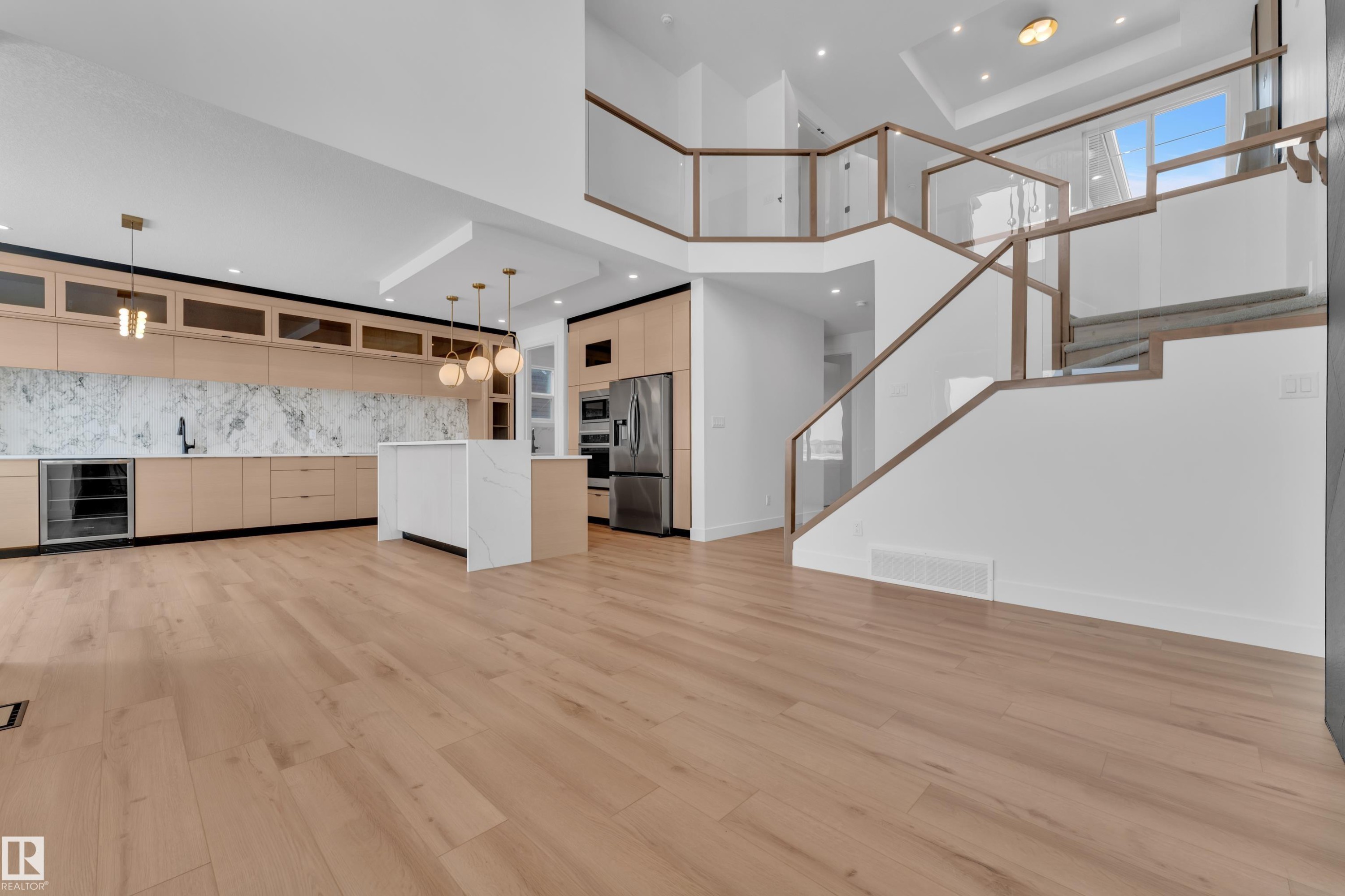 The open-concept living area features light wood flooring, a kitchen with light wood cabinetry, a white island, and a stainless steel refrigerator - 503 Creekside Bay, Leduc, AB - Indoor